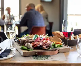 Image of a platter of a variety of fresh food accompanied with a bowl of bread and a glass each of red and white wine.