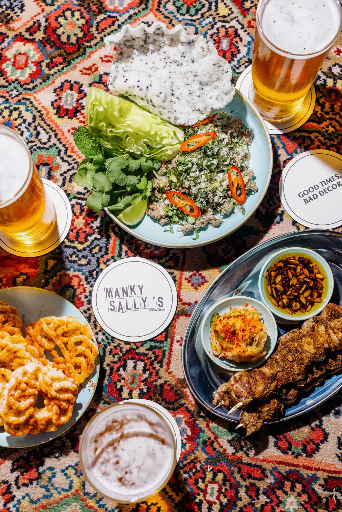 Beer, fried food and vegetables are plated and placed on a colourful, patterned, Persian-style carpet.