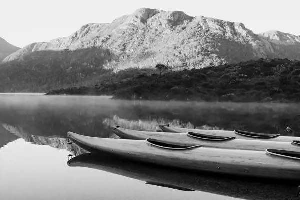 Wooden kayaks float on still, crystal-clear water on Dove Lake, with snow-covered mountain in the background.