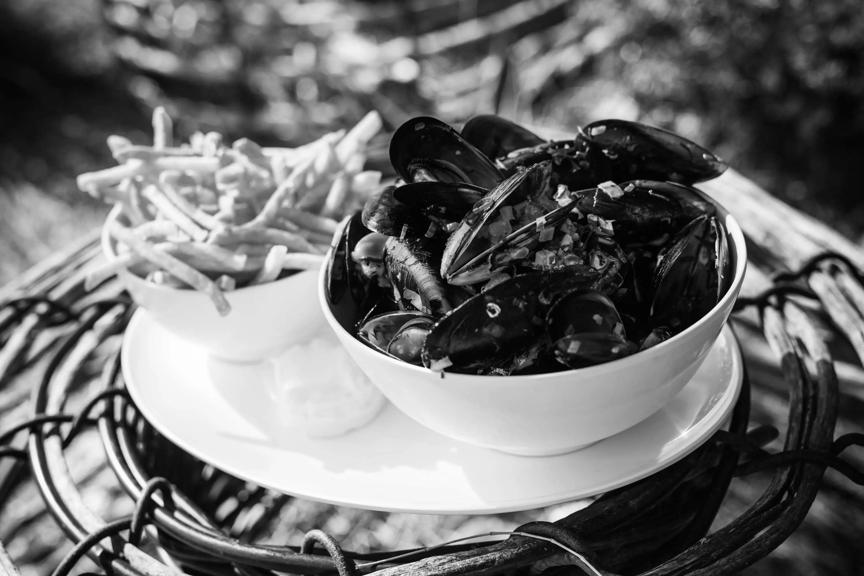 A bowl of black shelled mussels and freshly fried chips presented in the top of a crayfish pot made of curved wood and fastened with wire.
