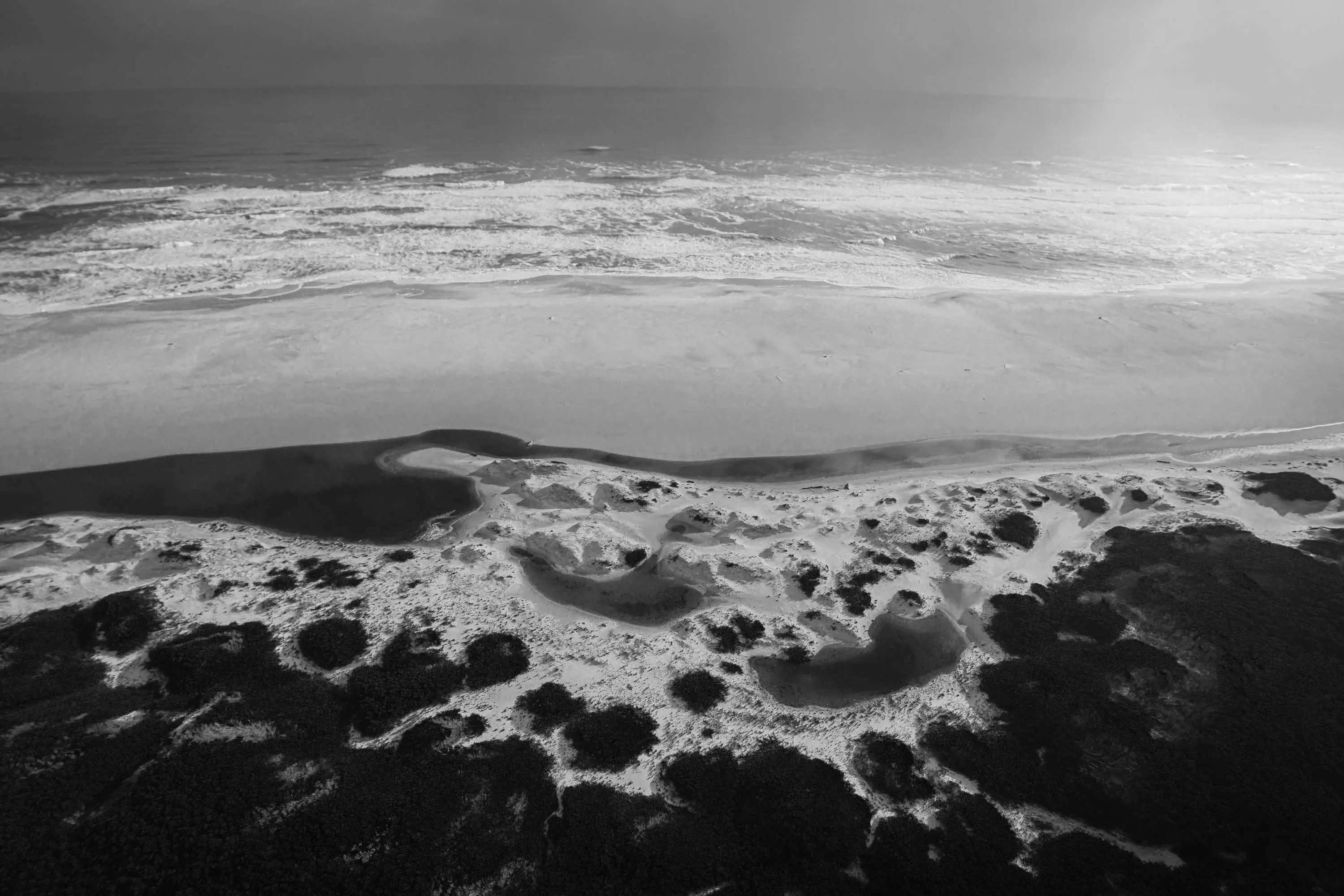 An aerial photograph of a water crashing onto a vast, sandy beach near the coast. 