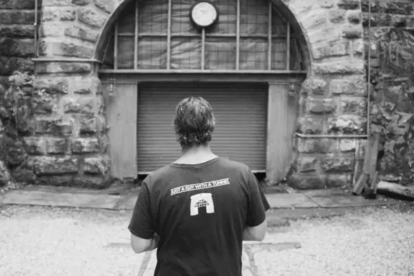 A man wearing a dark t-shirt that reads 'just a guy with a tunnel' on the back, walks towards a tunnel entrance. 
