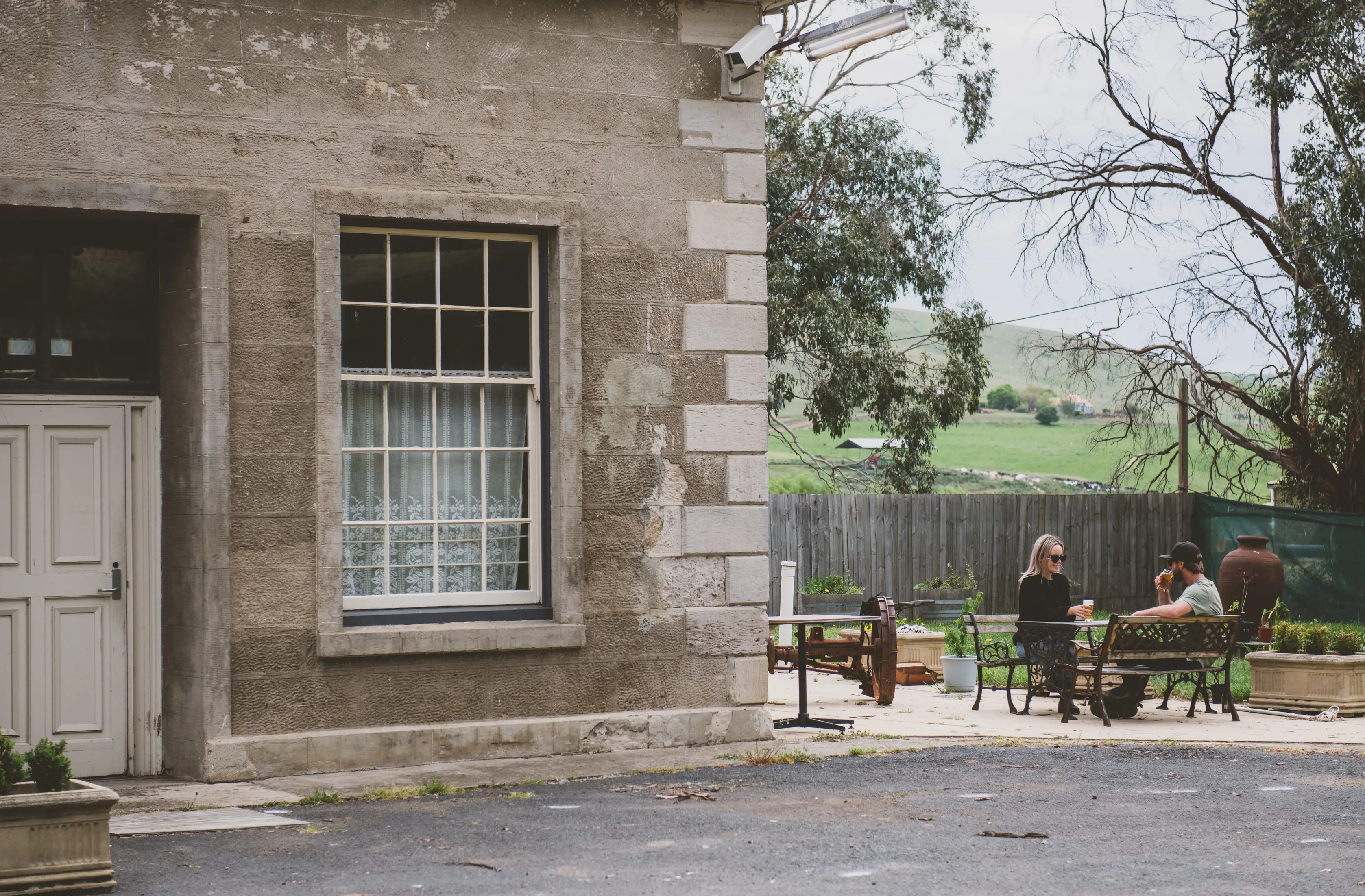 Exterior image of Hamilton Inn, cellar door, cafe & accommodation, convict built in 1826. People enjoy refreshments on a bench outside.