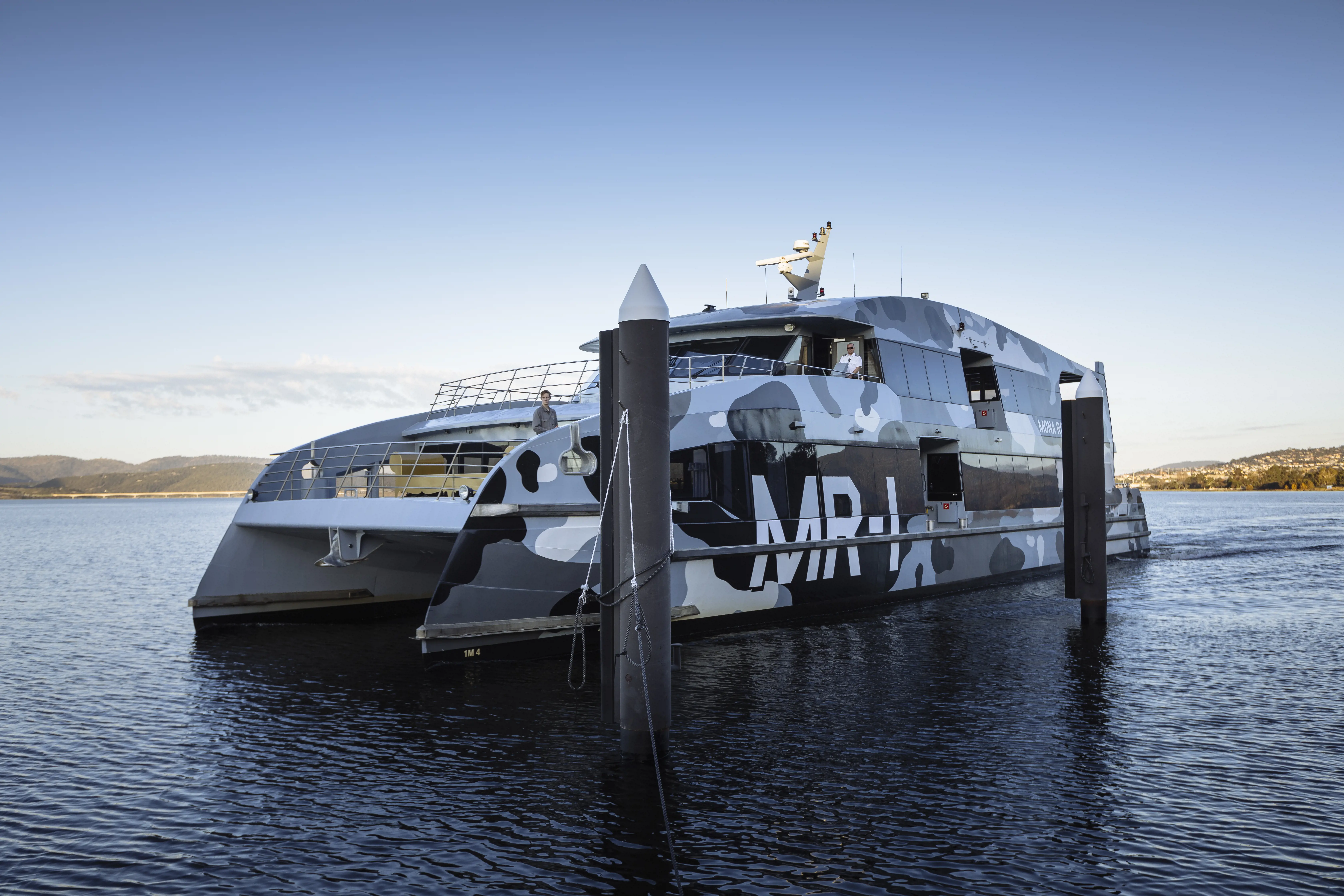 A modern catamaran with a black and white camouflage pattern sitting on still water.