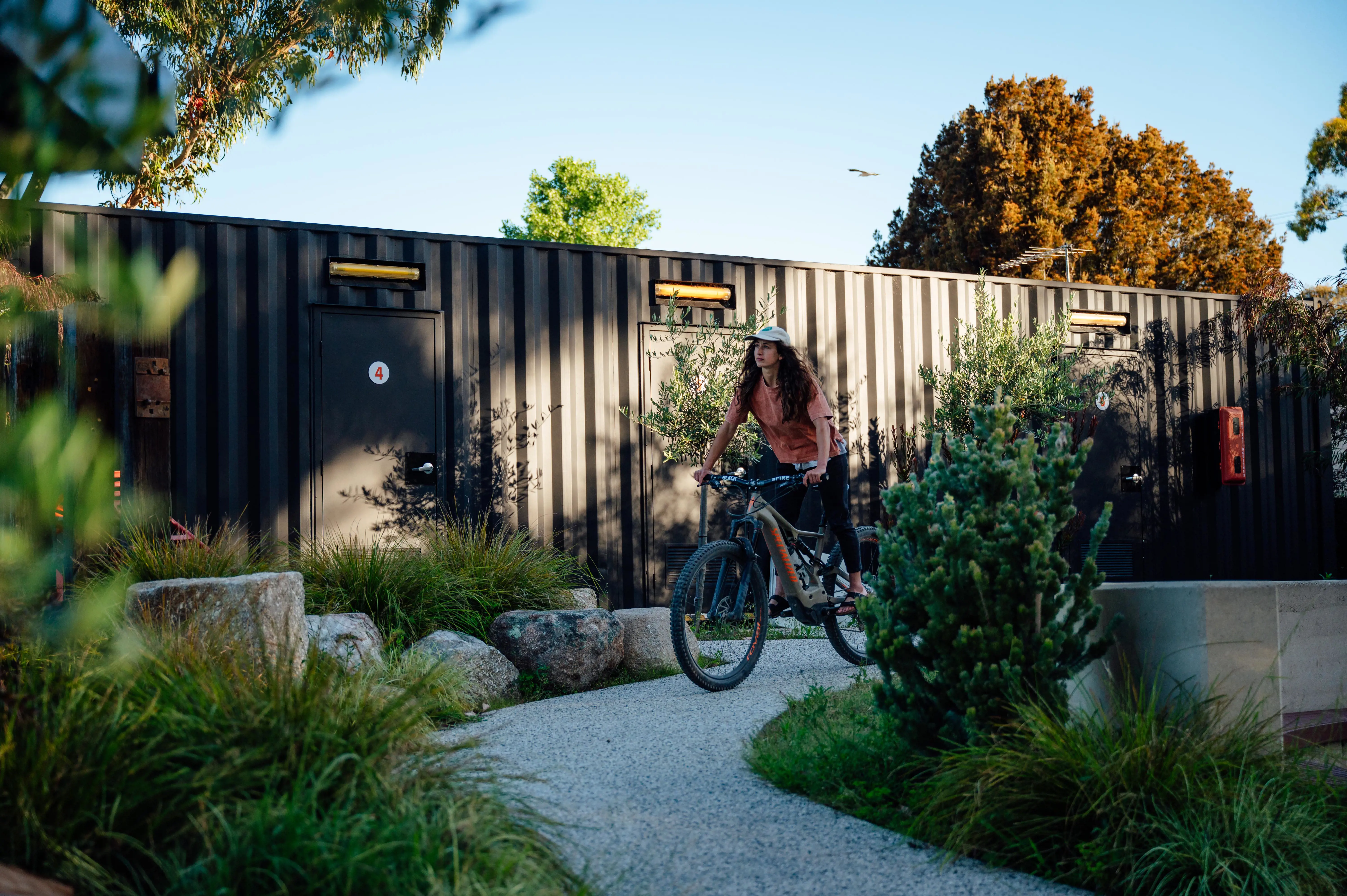 A young woman rides a mountain bike on a gravel path through a native plant garden.