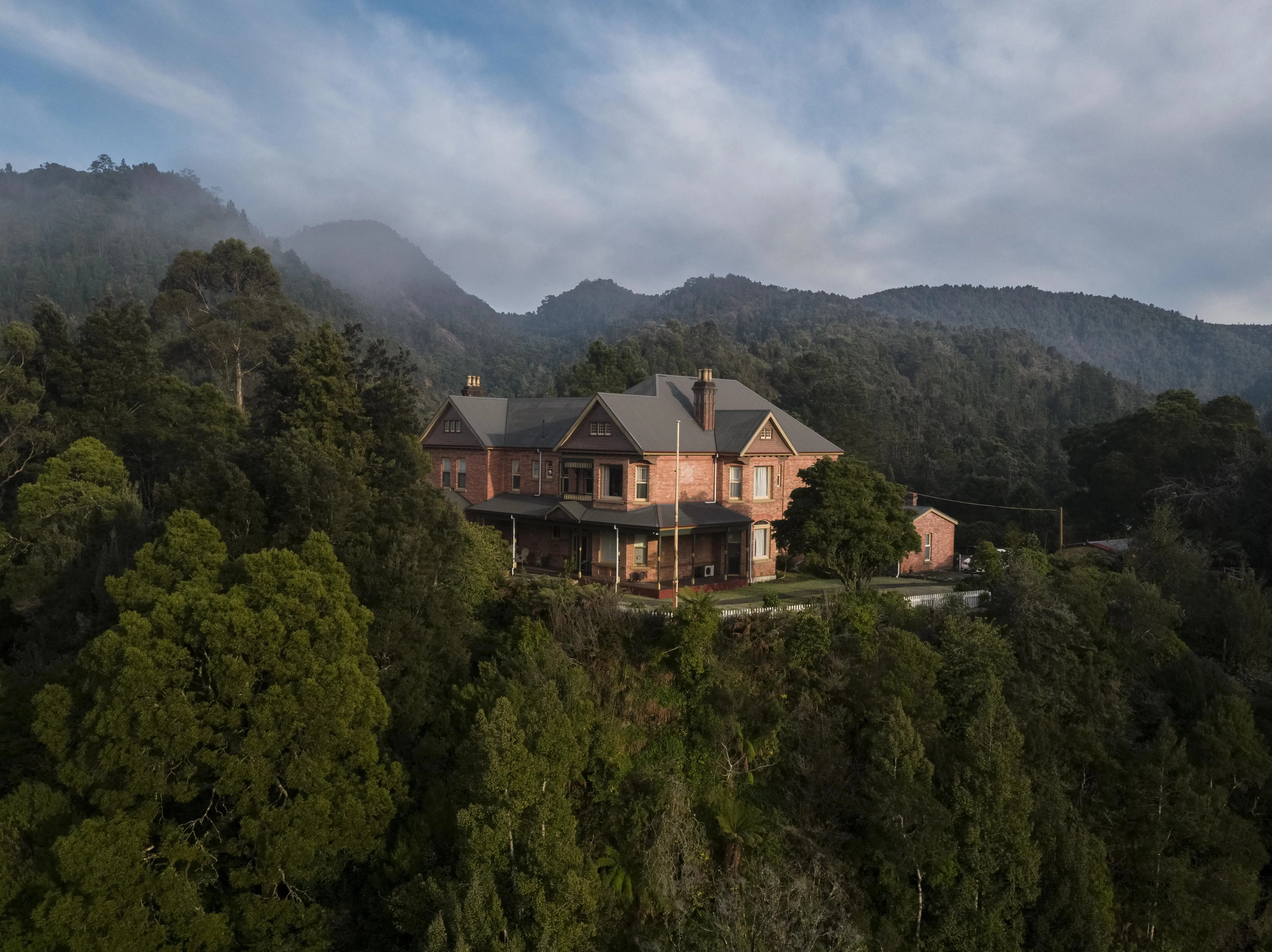 A heritage brick building stands on an elevated clearing amongst dense forest.