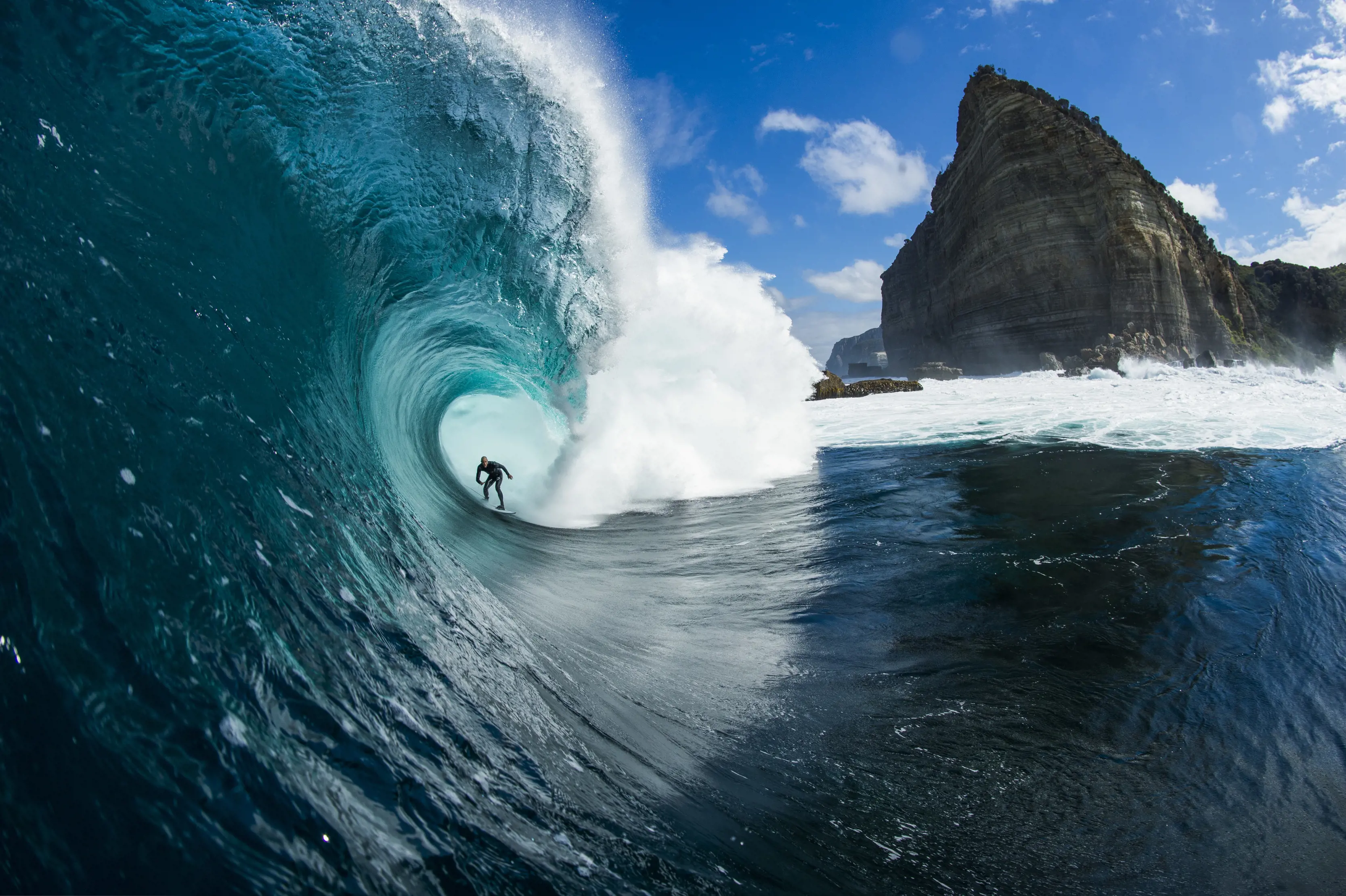 Looking down at a surfer getting barrelled by a large wave, with a prominent headland in the background, at Shipsterns Bluff, Tasman National Park.