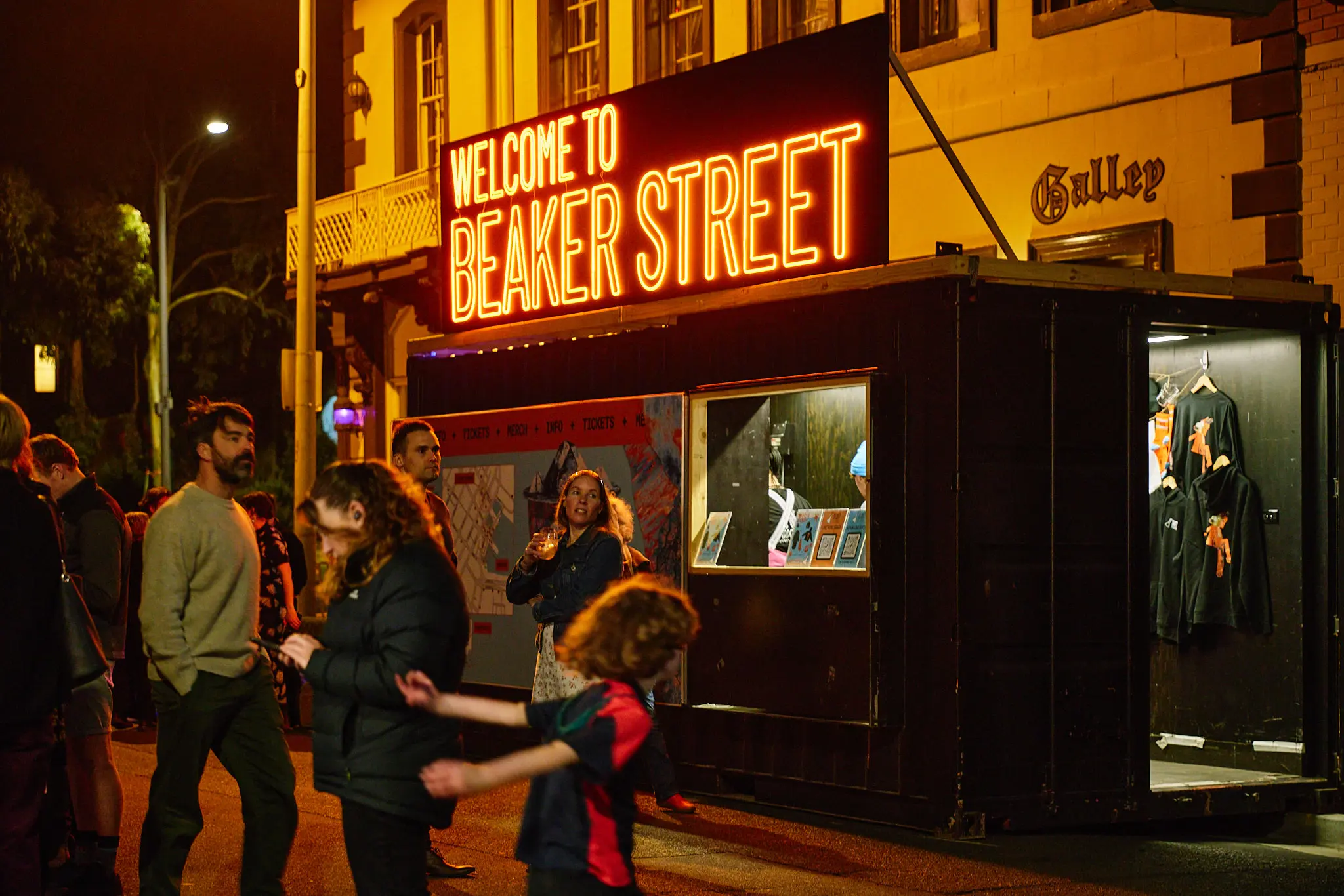 Night scene shows an illuminated entrance with "Welcome to Beaker Street" signage. People gather outside the lit venue on the street.