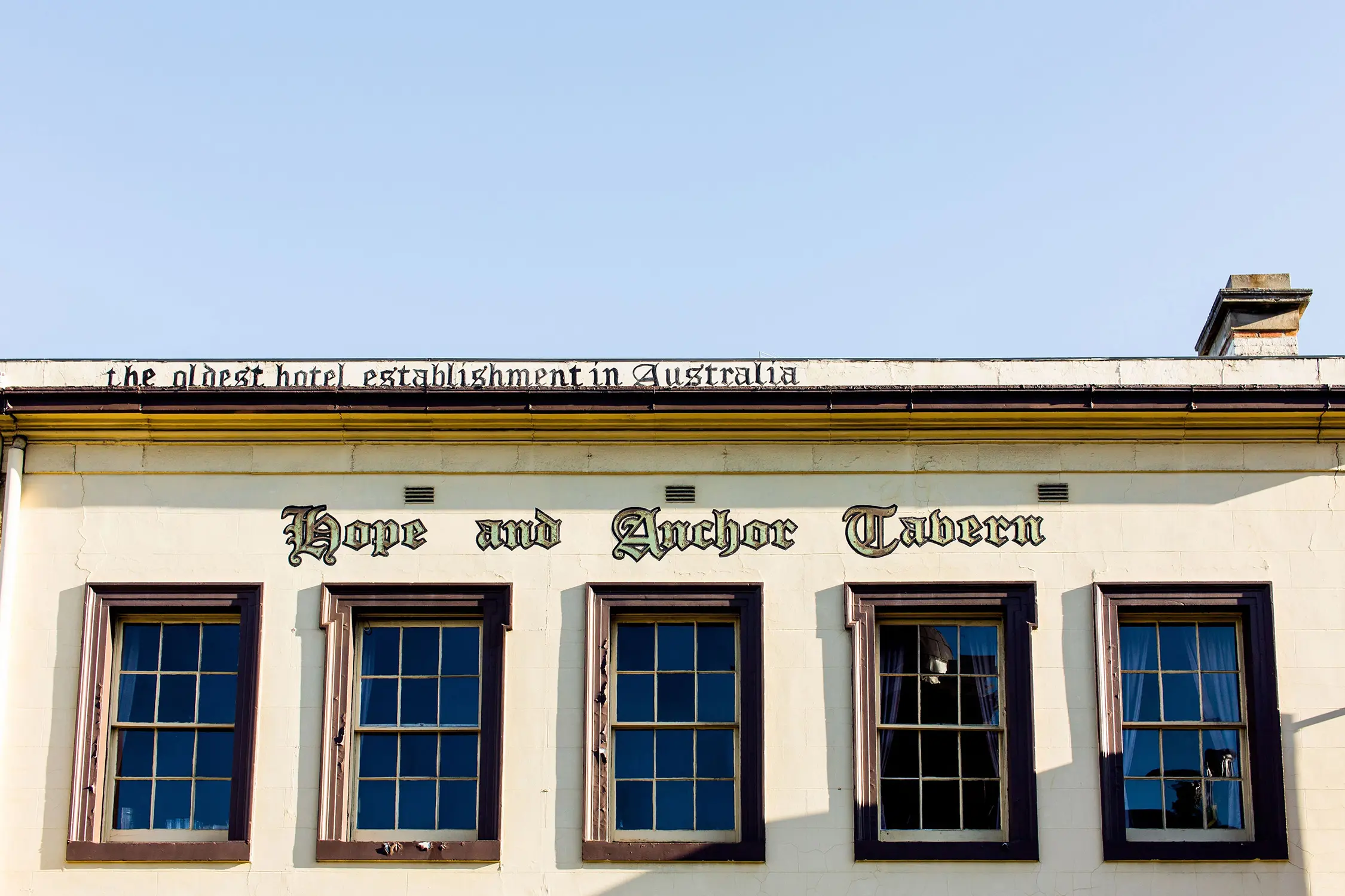 A heritage building with a cream and red facade features five blue windows arranged in a row, and "Hope and Anchor Tavern" printed in medieval lettering.