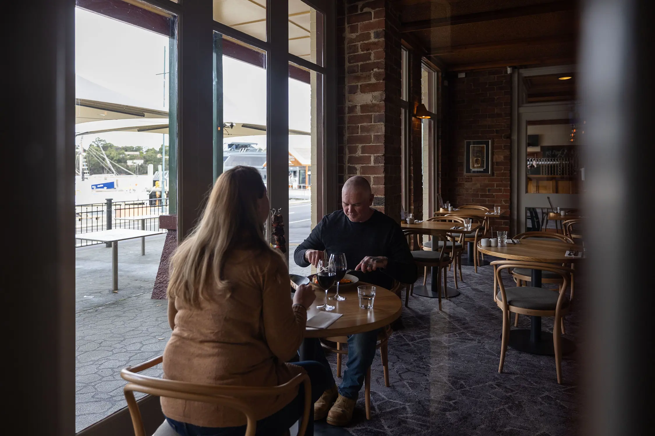 Diners sit at wooden tables inside a sleek restaurant with marble floor and exposed brick walls.