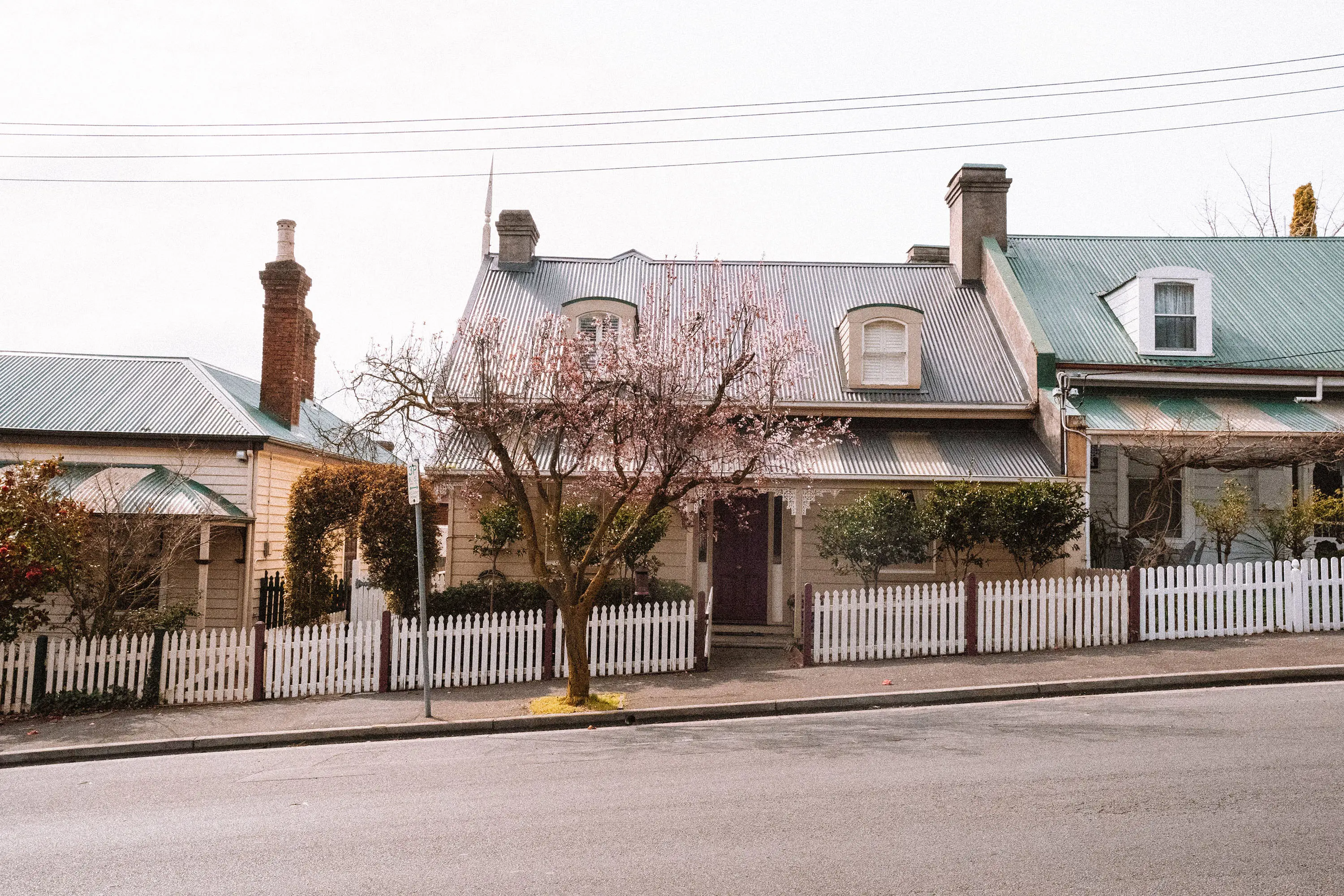 A row of heritage cottages on a slightly sloped street, with historic details like wrought iron decorations and white picket fences.