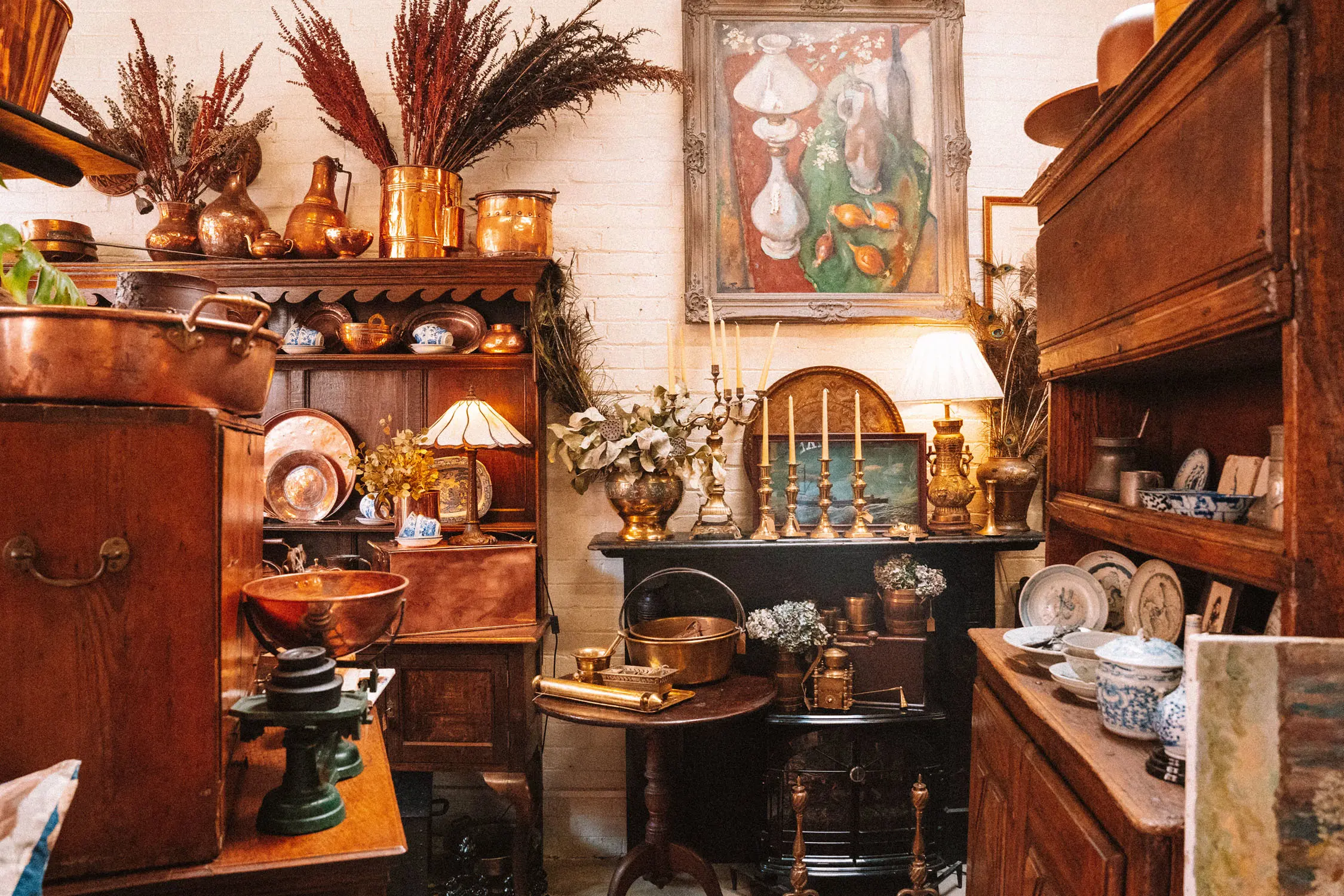 The corner of an antiques store, with several warm wooden cabinets displaying crockery, candleholders, baskets and other vintage treasures.