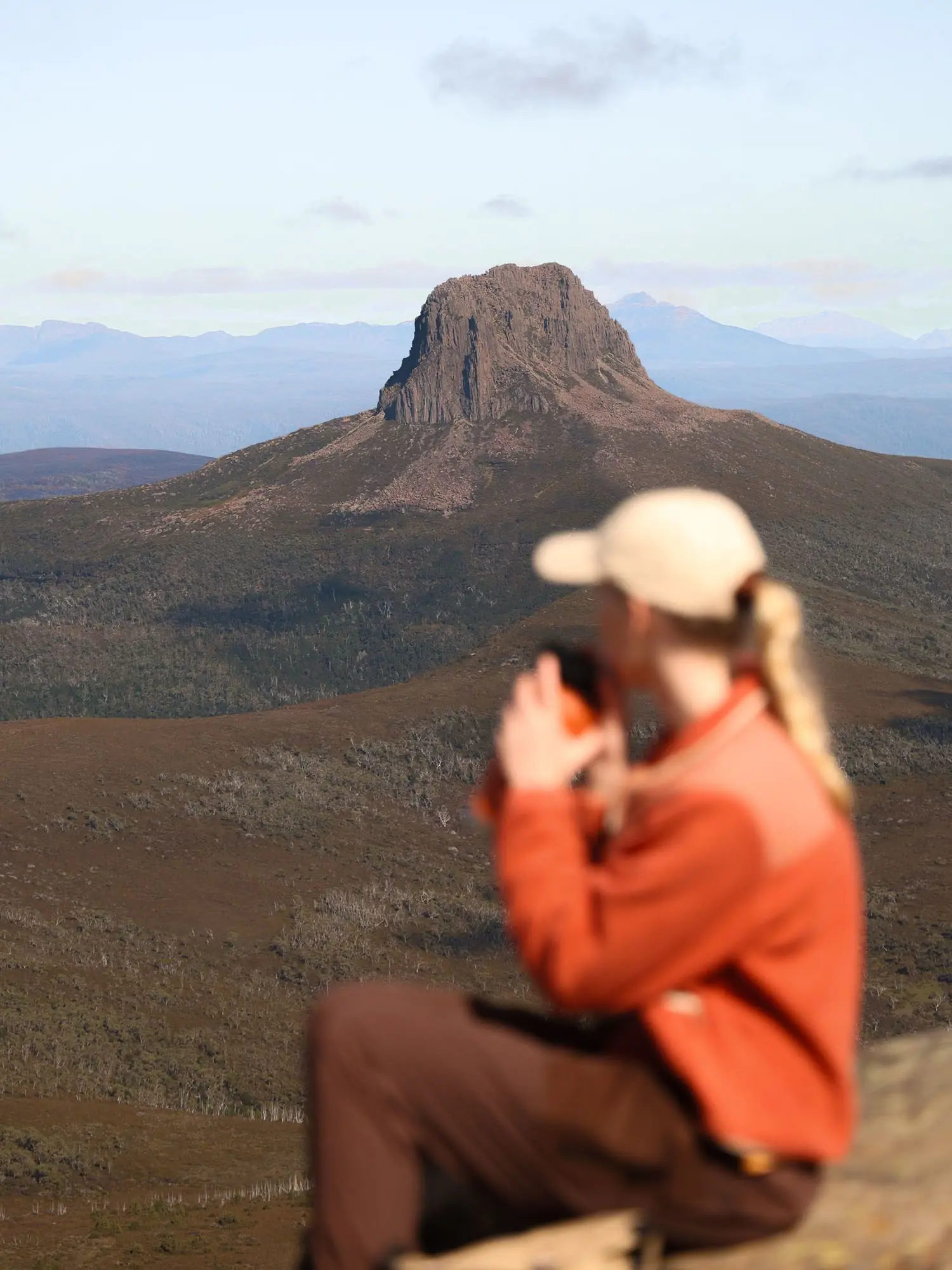 A woman in hiking clothes is sitting on a rock looking out towards Barn Bluff in the distance.