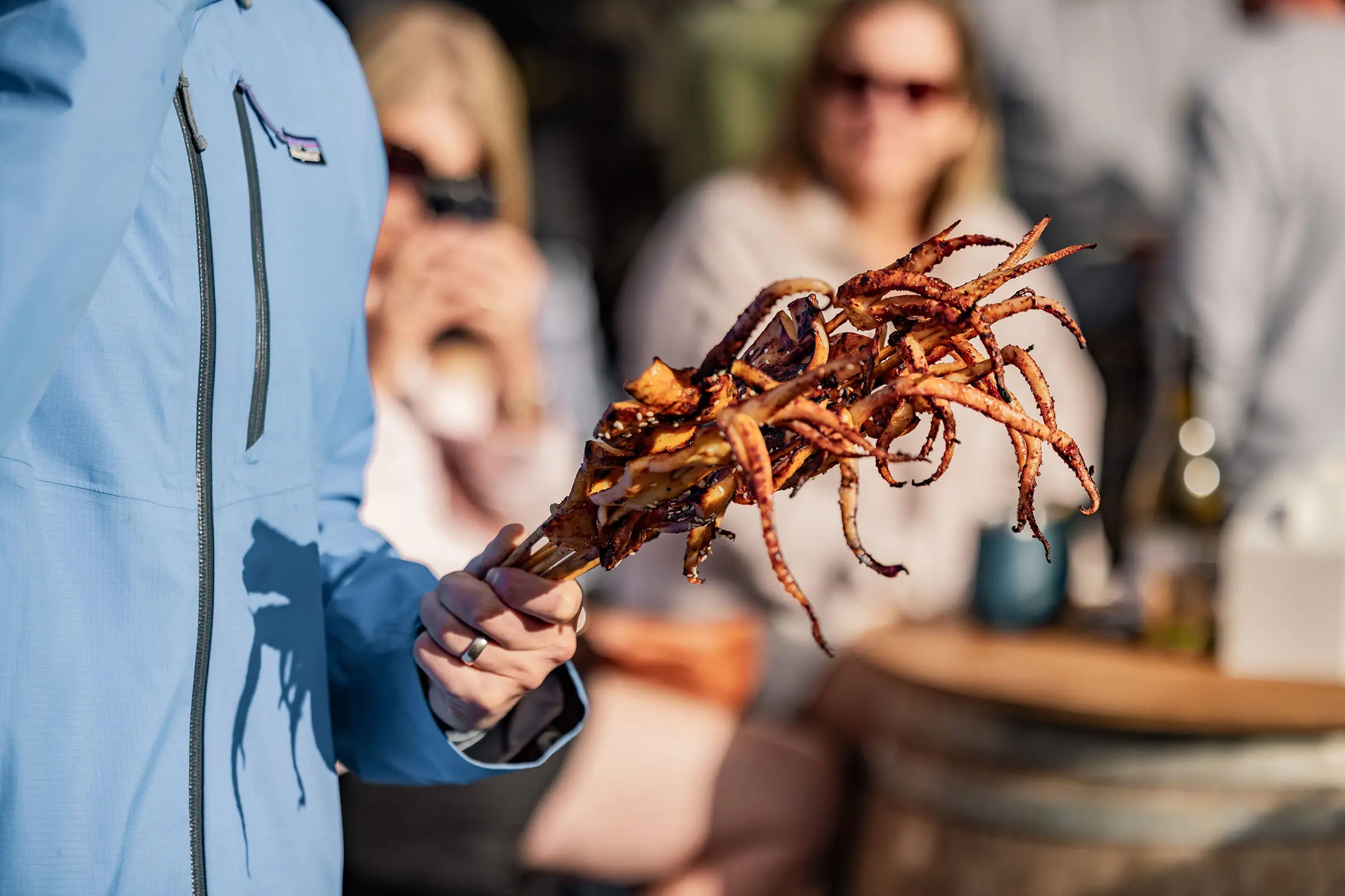 A person holds a handful of skewers of marinated squid, with the roasted tentacles coming out at crazy angles.