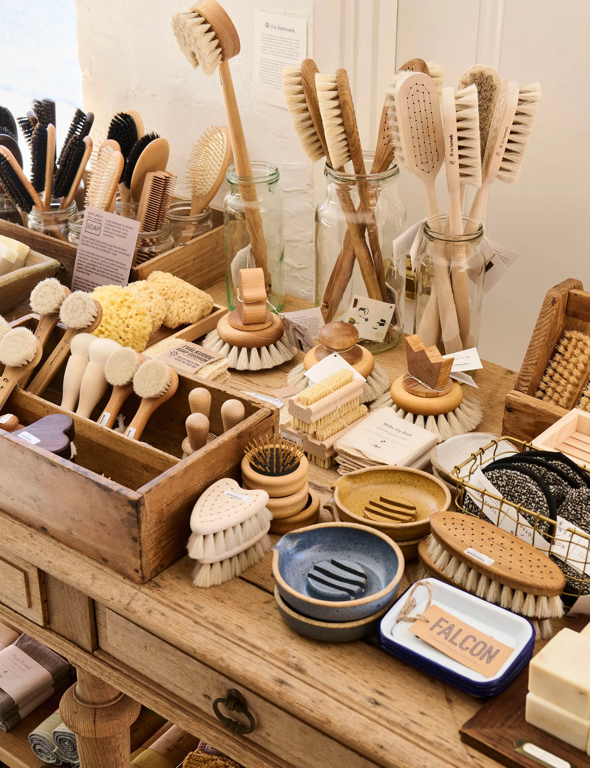 A collection of quality wooden and ceramic cleaning and home care supplies, like brushes stacked in jars and handmade soap dishes.
