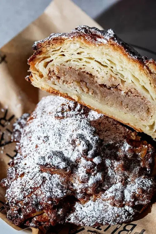 A close up image of an almond croissant sitting on a piece of brown paper, cut in half to reveal flaky layers and frangipane filling.