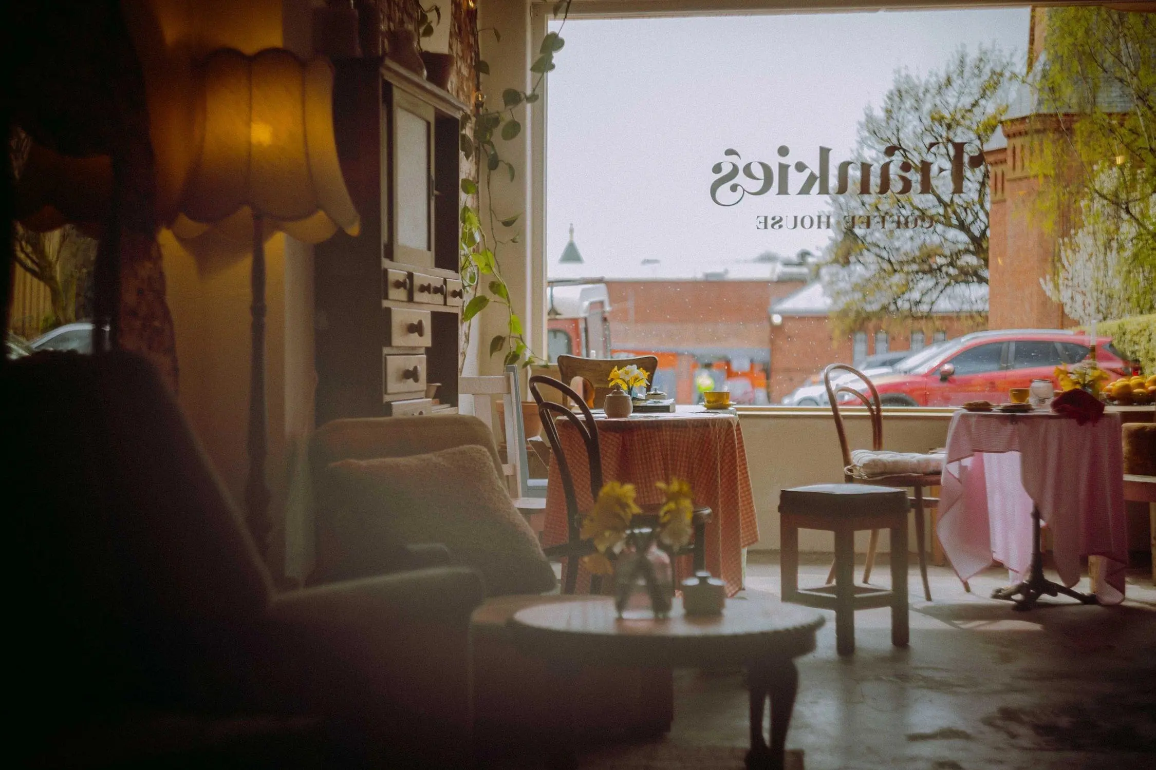 The interior of a cosy cafe, with cute mismatched furniture, soft lighting, plants and draped tablecloths.