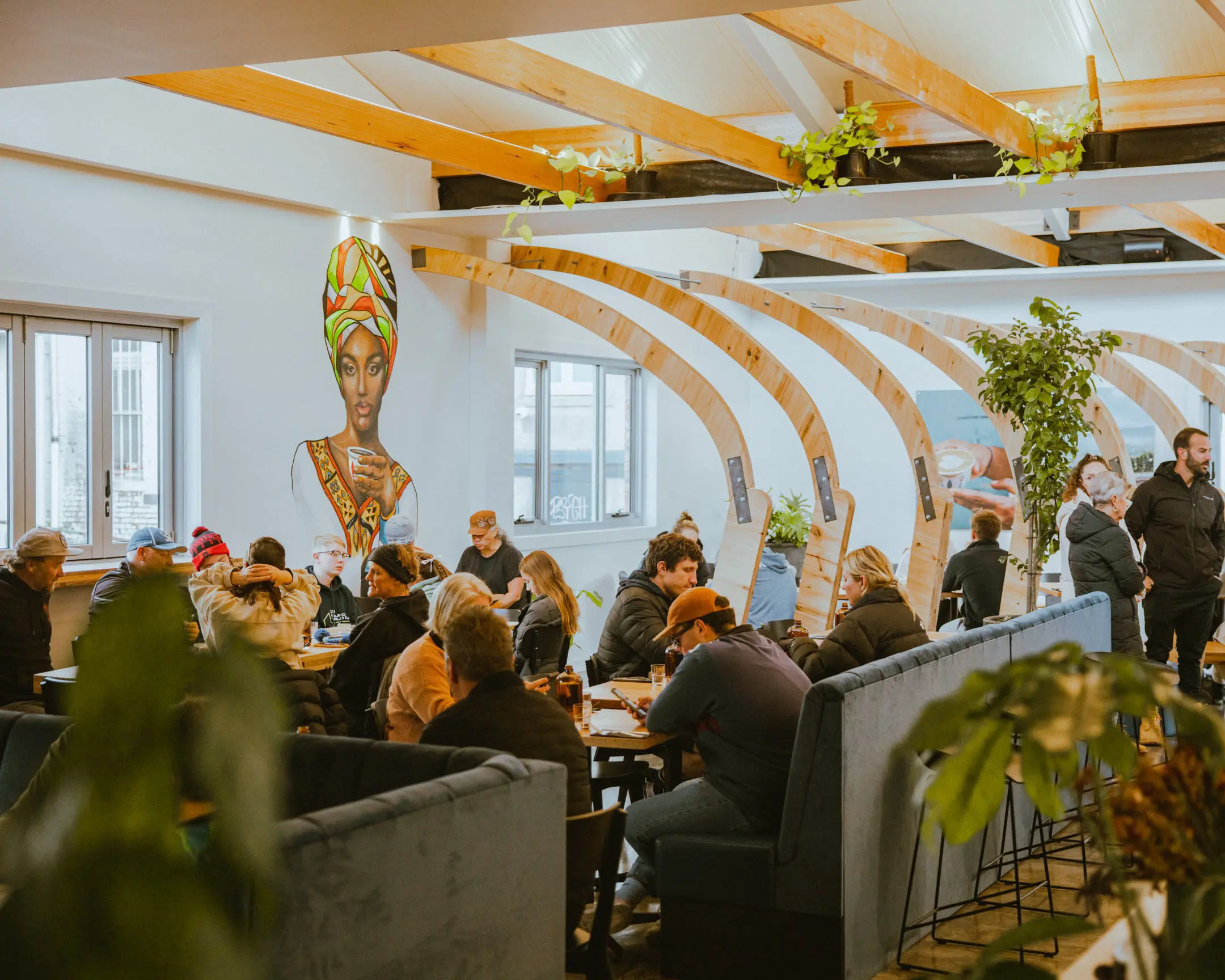 The light-filled interior of a busy coffee shop, with a large mural of an African woman drinking coffee on one wall.