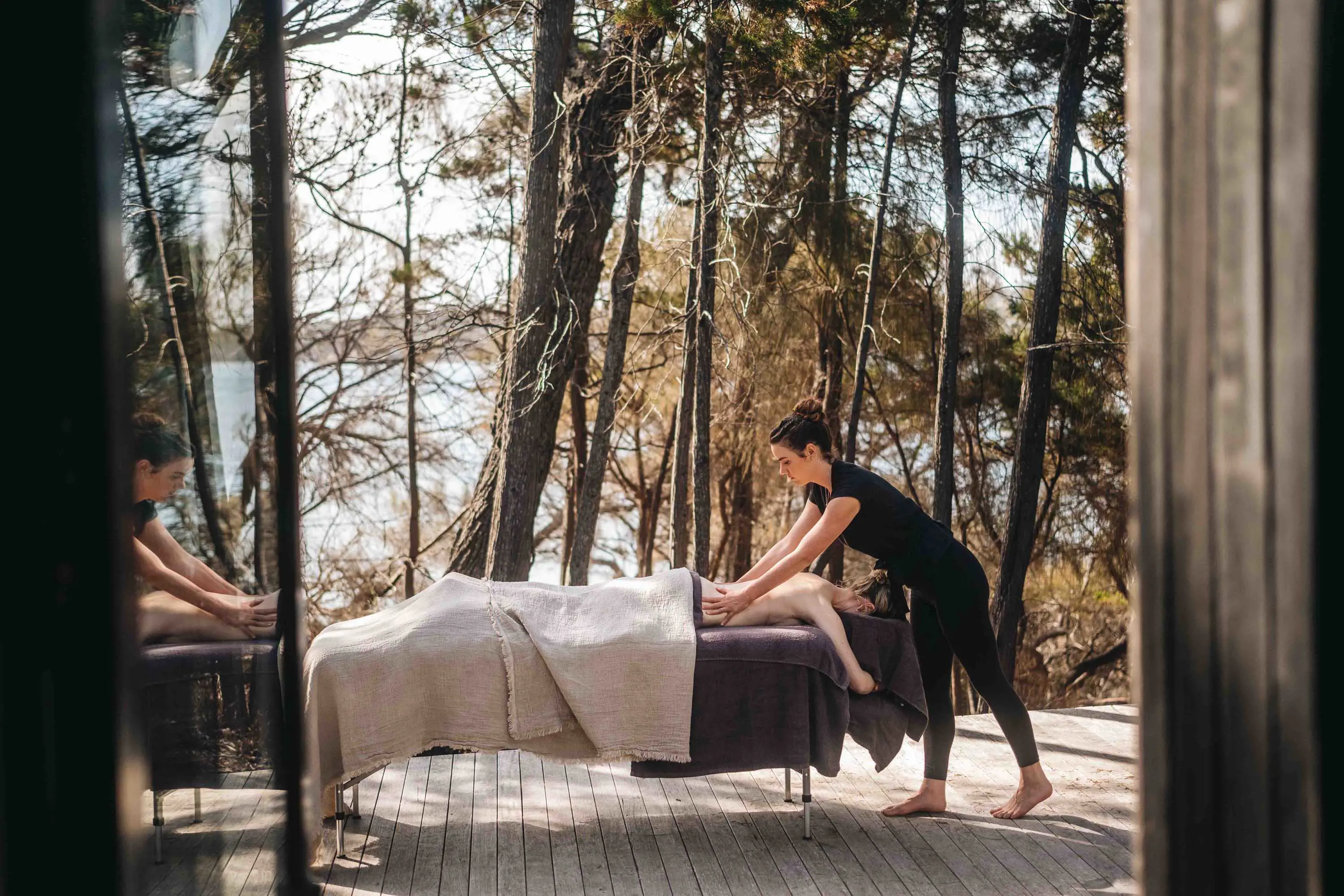 A woman lies on a large outdoor trestle table and has a back massage.