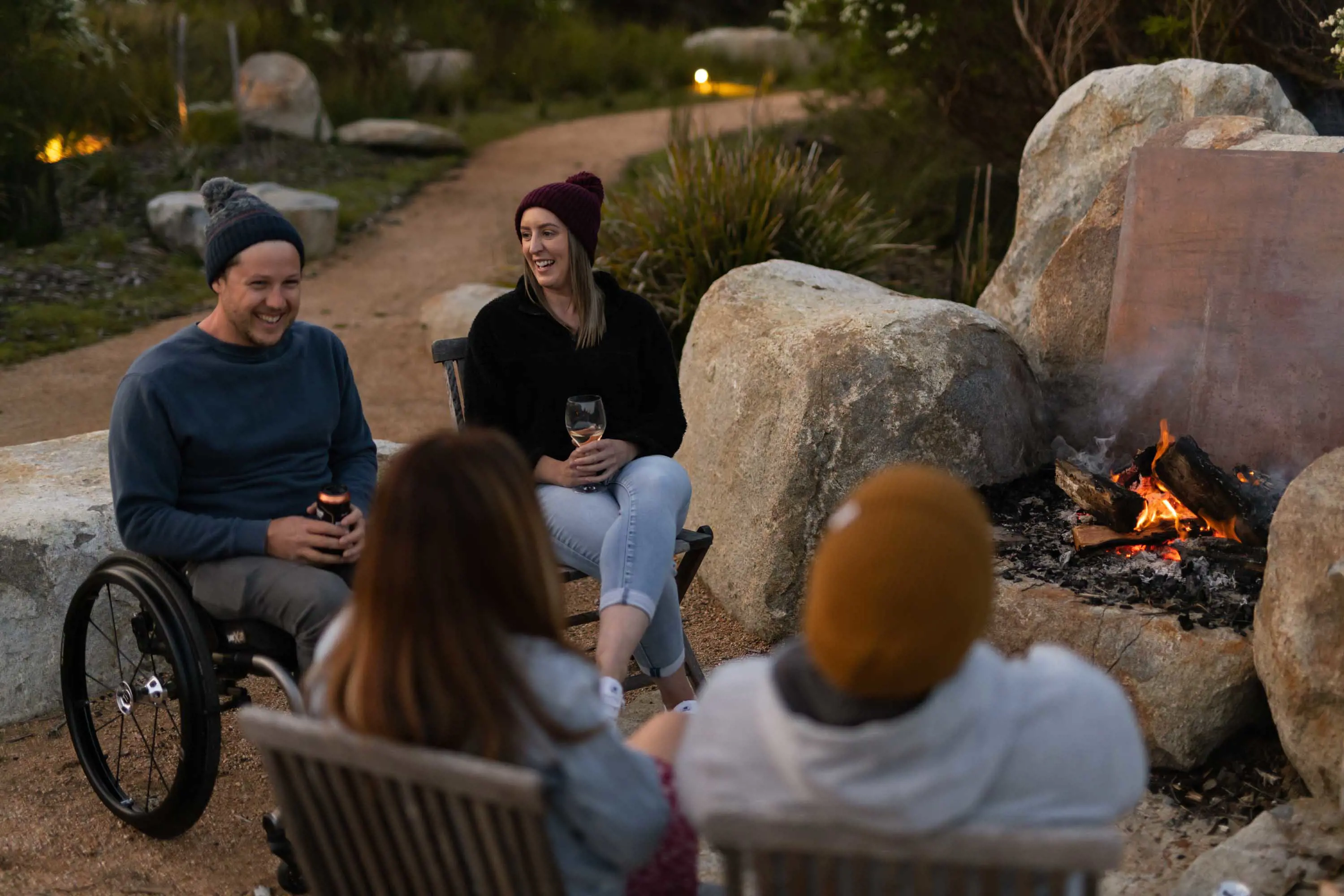 A group of people wearing beanies gather around a campfire wearing beanies and chatting.