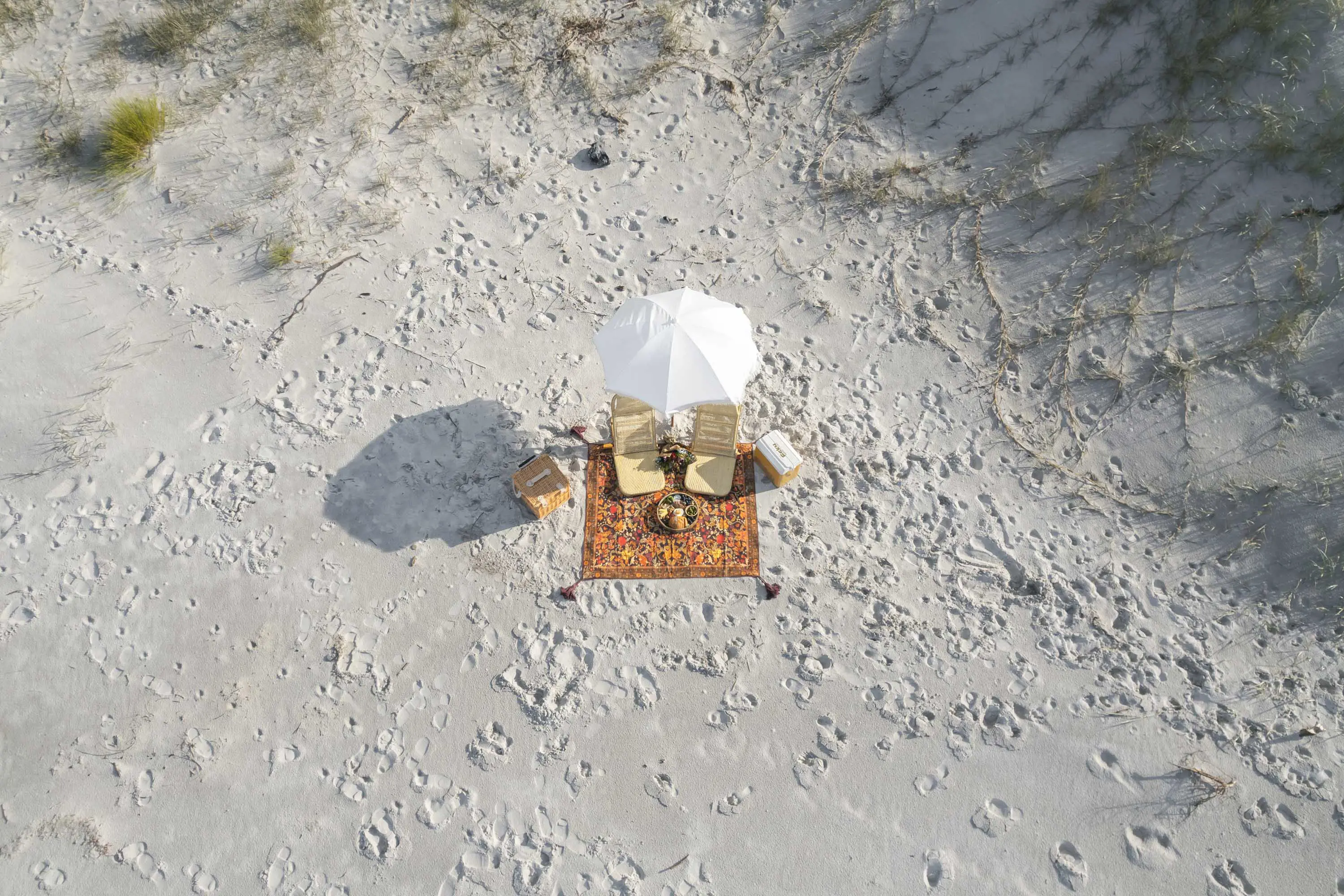 A picnic rug with two chairs sit under a large white umbrella on a white sand beach.