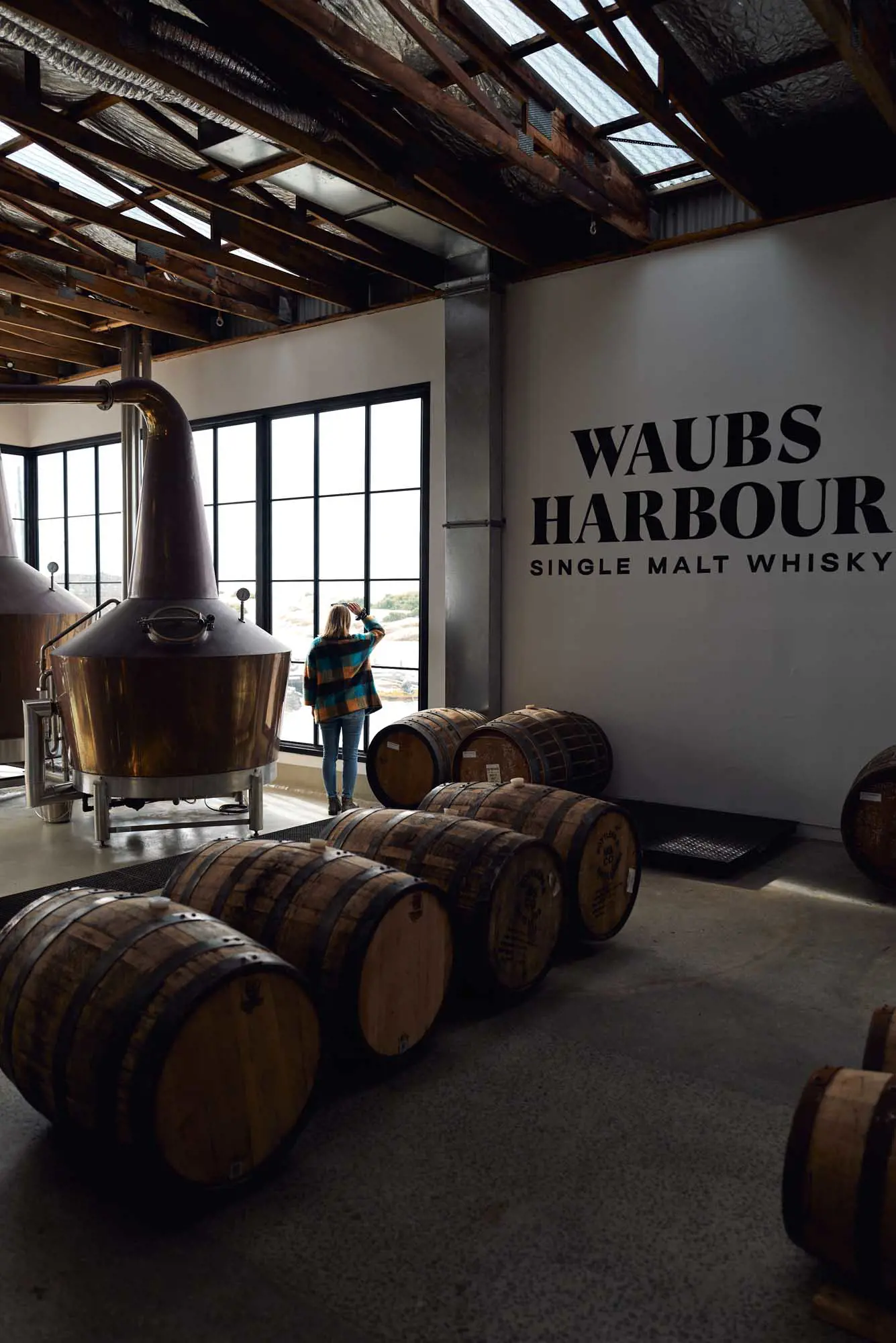 A high-ceiling industrial warehouse converted into a distillery with large copper stills and windows.