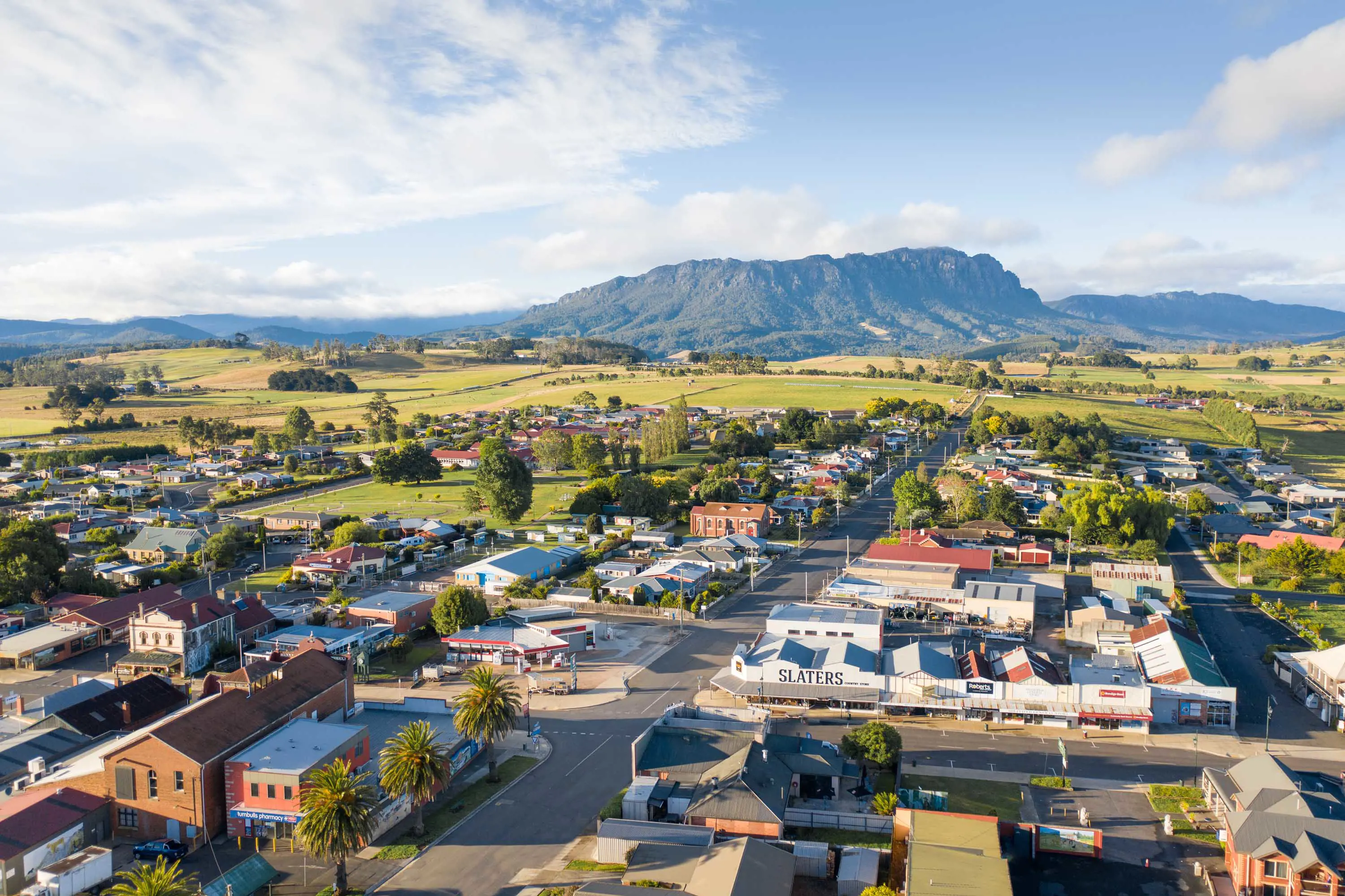 An elevated view of a small, country town with wide streets set in the shadow of a large range of mountains.
