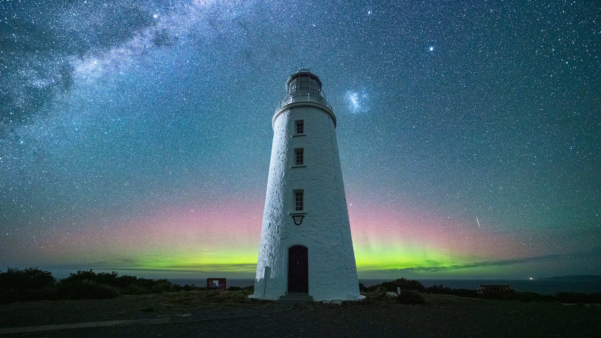Picturesque image of Cape Bruny Lighthouse with the Aurora Australis illuminating the night sky green and pink.