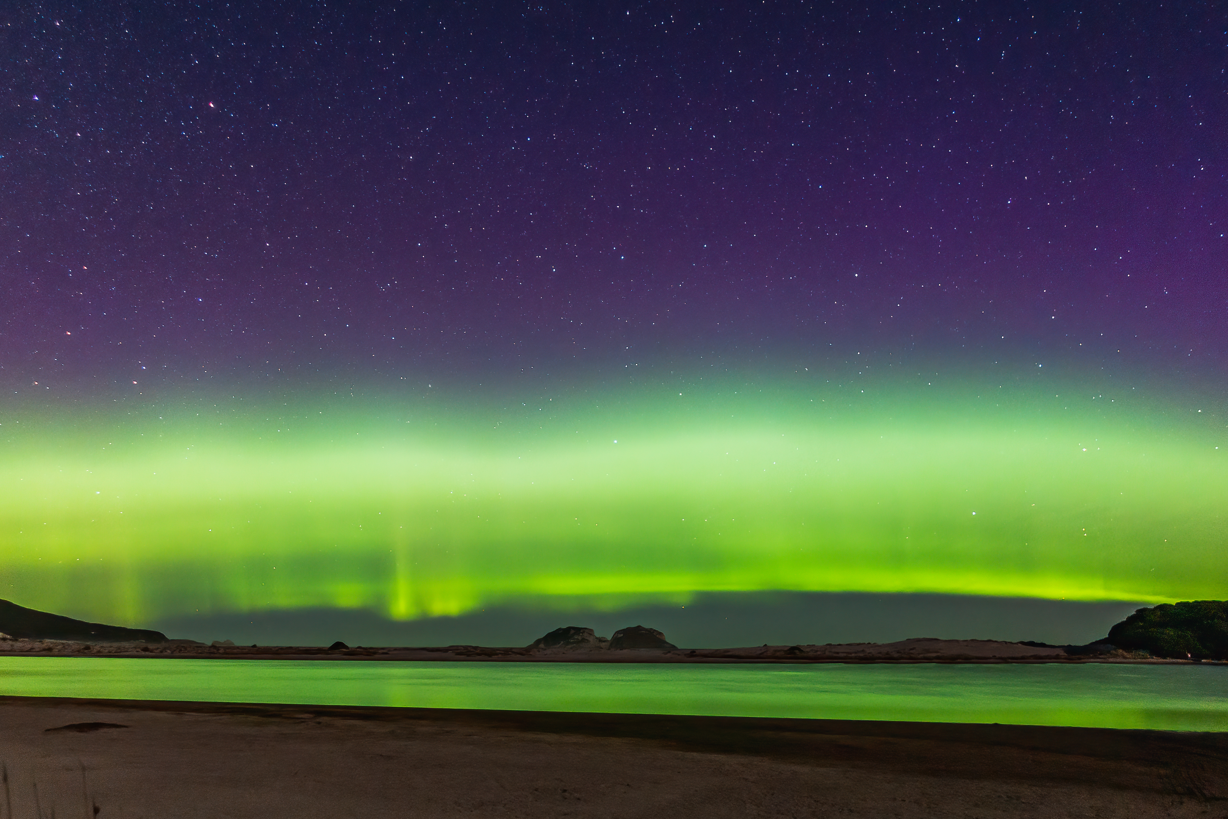 Beach glowing green reflecting the Aurora Australis along the South Coast Track.
