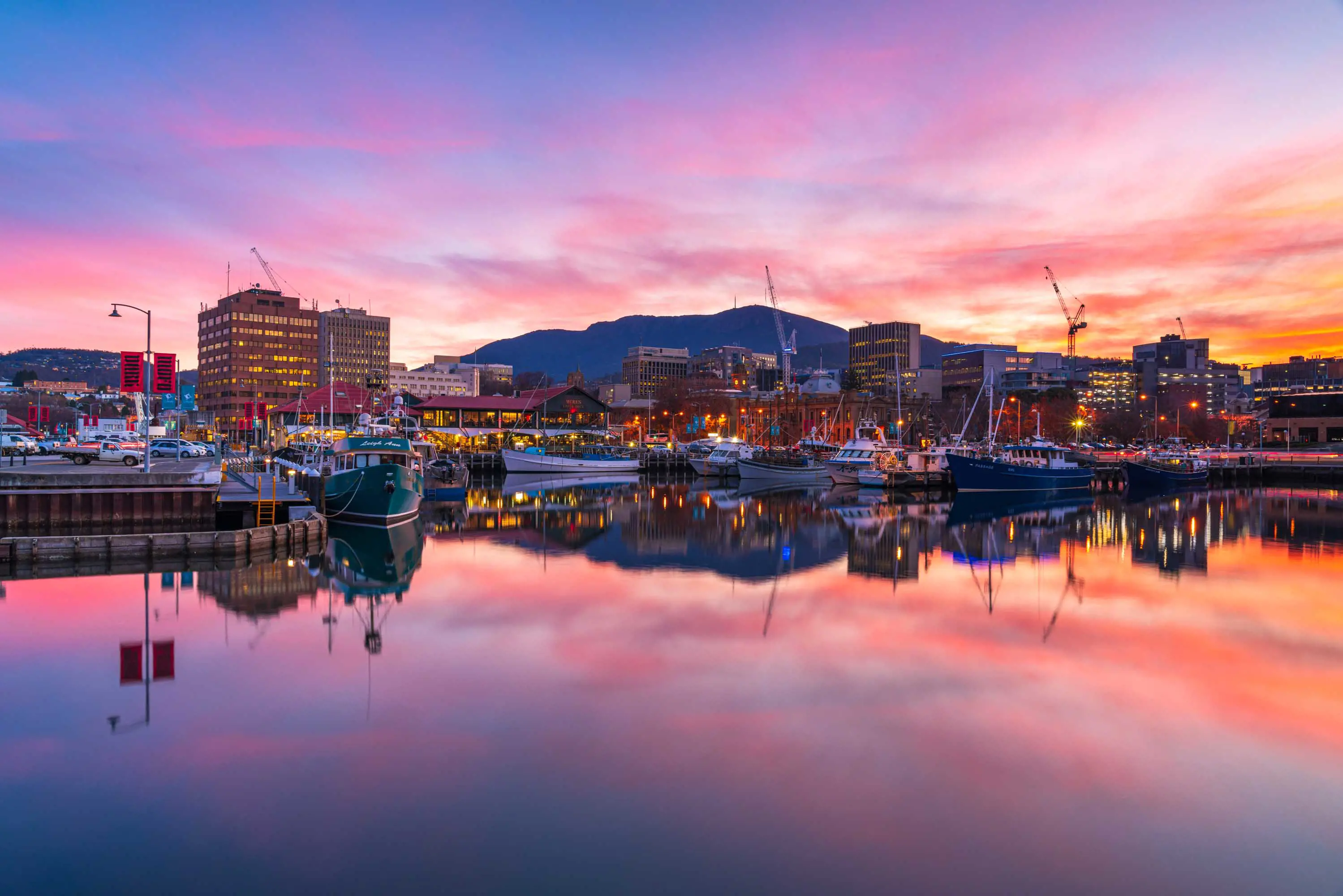 A pink sunset over the city lights of Hobart reflected in water at the waterfront.