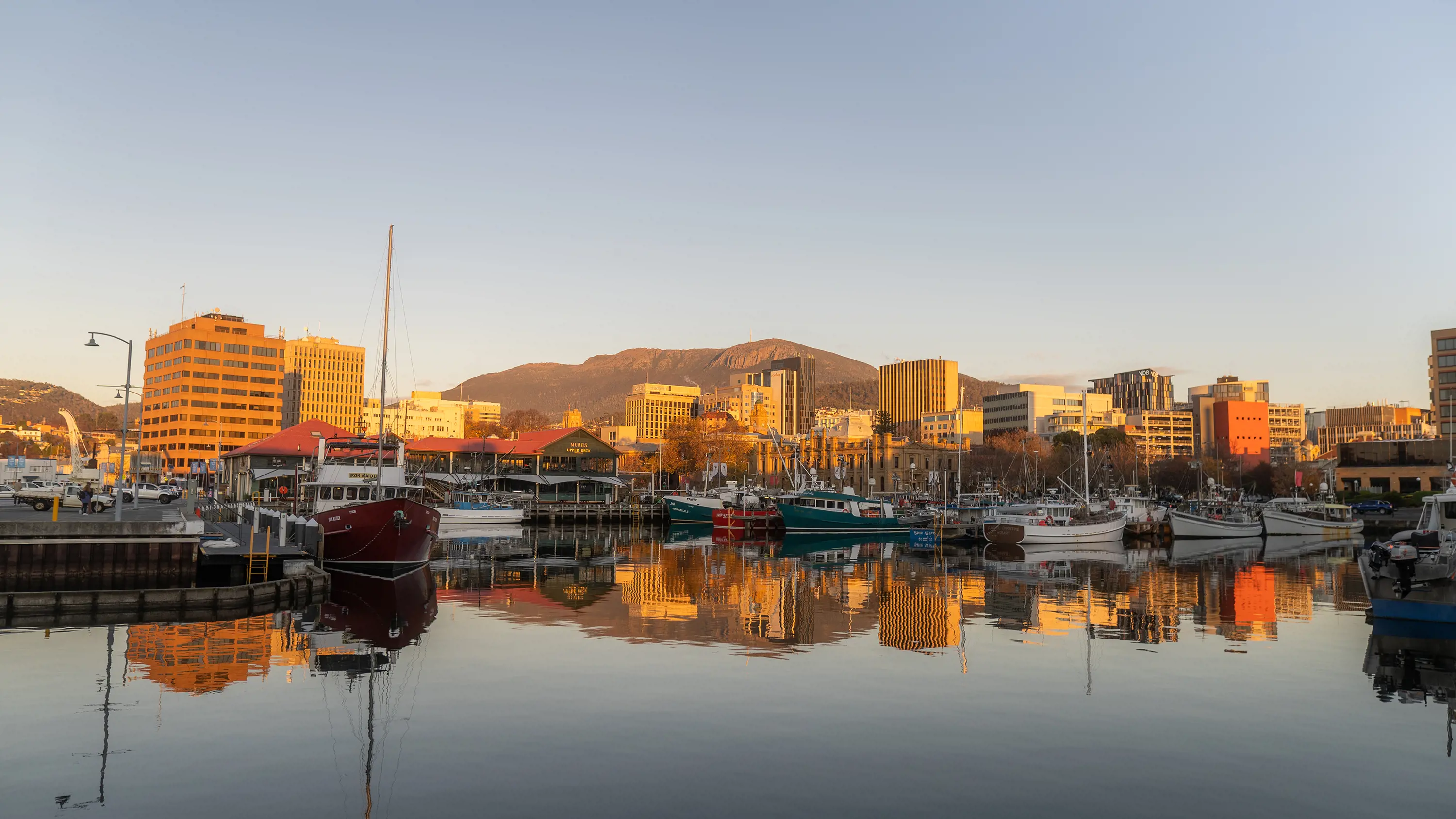 Hobart city at sunrise, reflected in the water of the waterfront on a clear day.