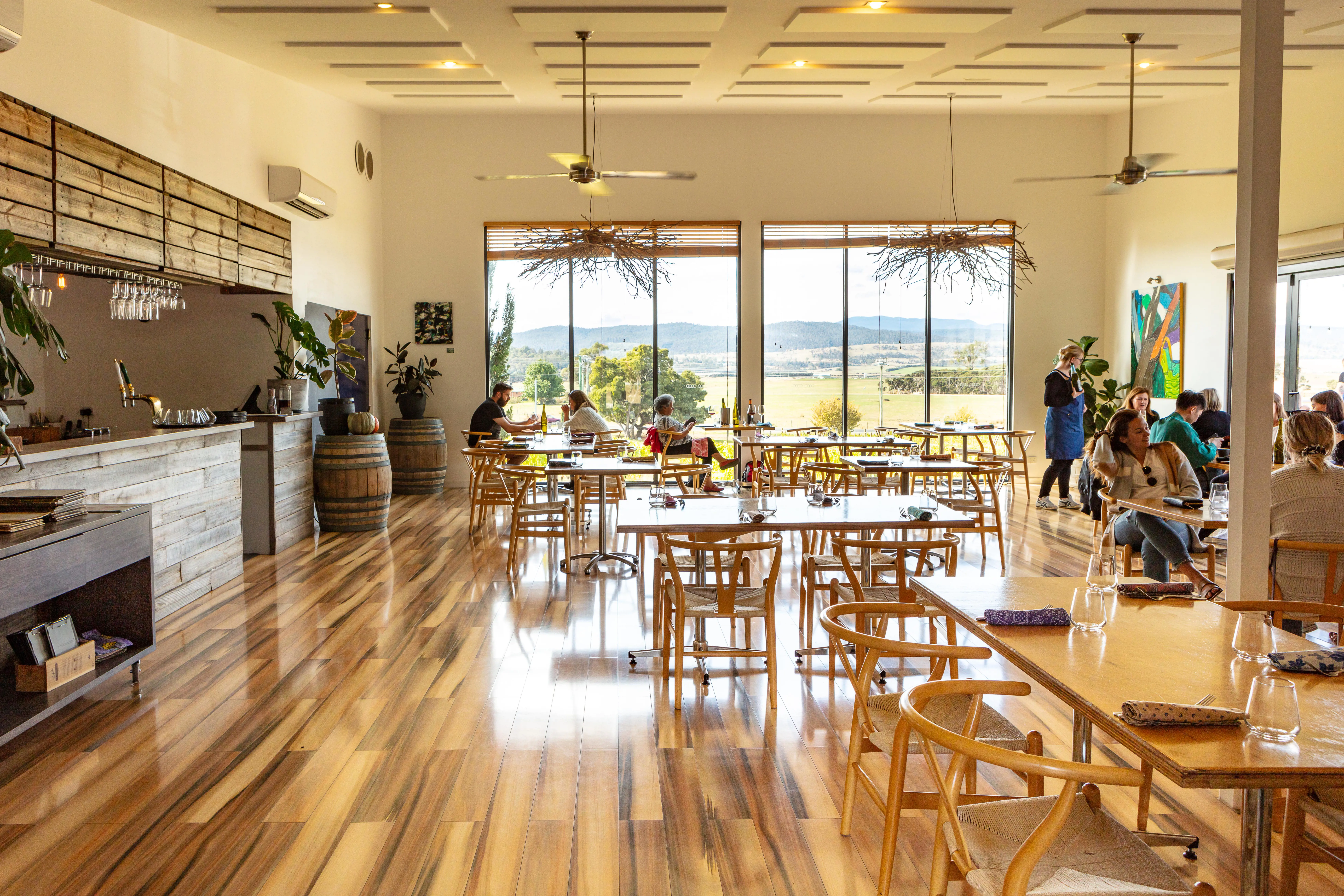 A dining room with wooden floors, and large windows looks out over rolling hills at the Velo Wines vineyard.