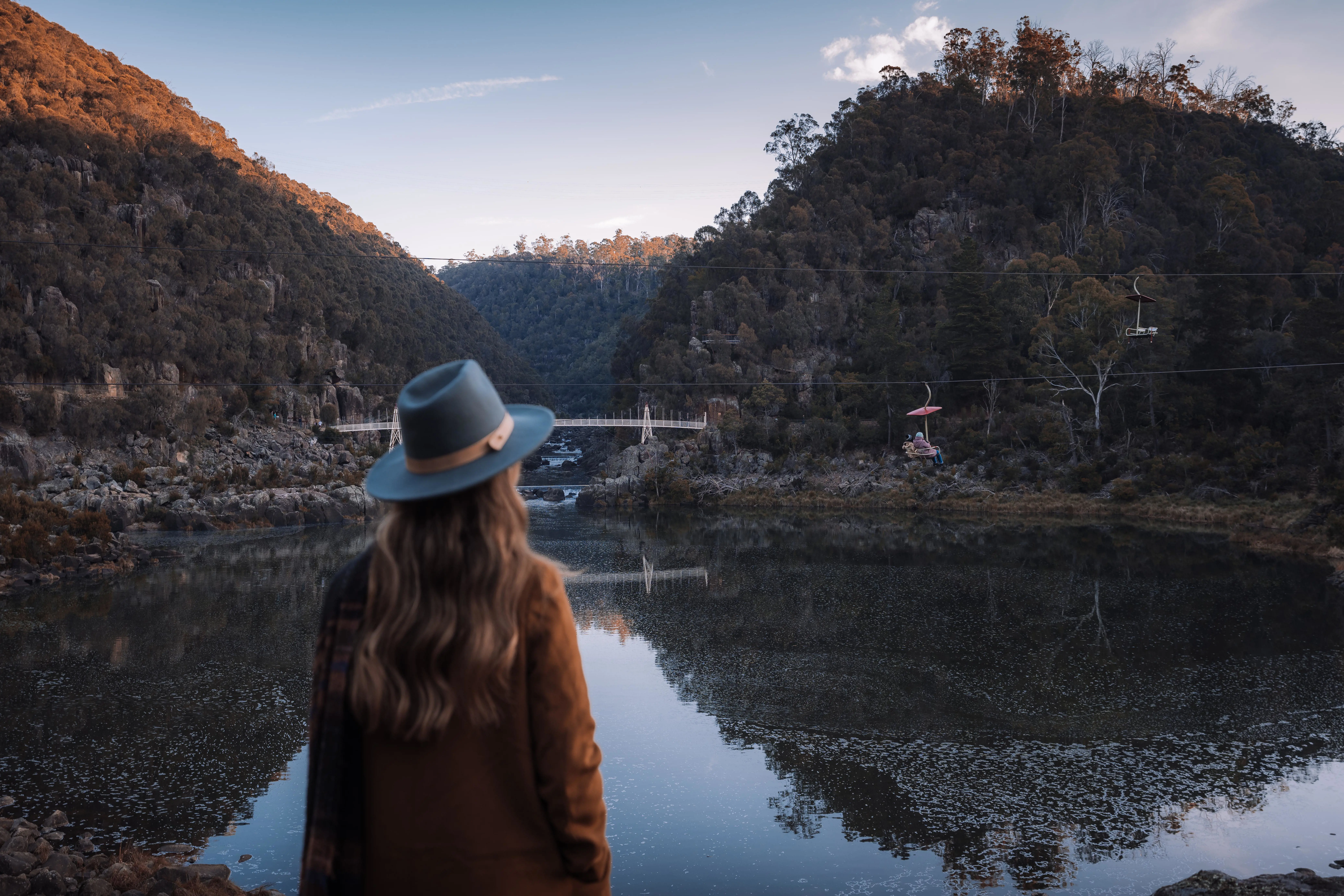 A young woman wearing a wide-brimmed hat looks out over the glassy water of Cataract Gorge.