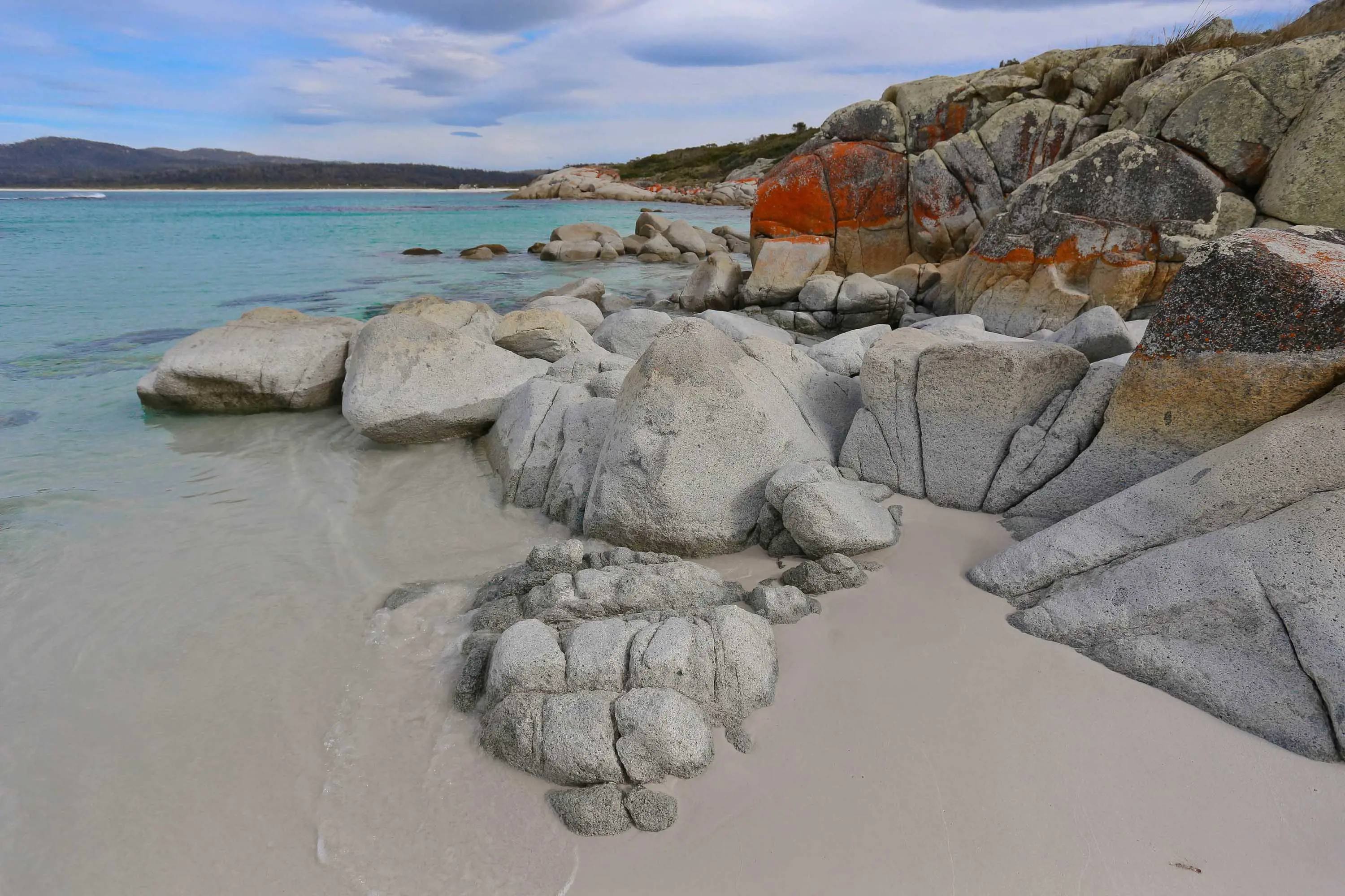 White rocks capped with orange lichen lead into the light blue waters on the east coast of Tasmania.