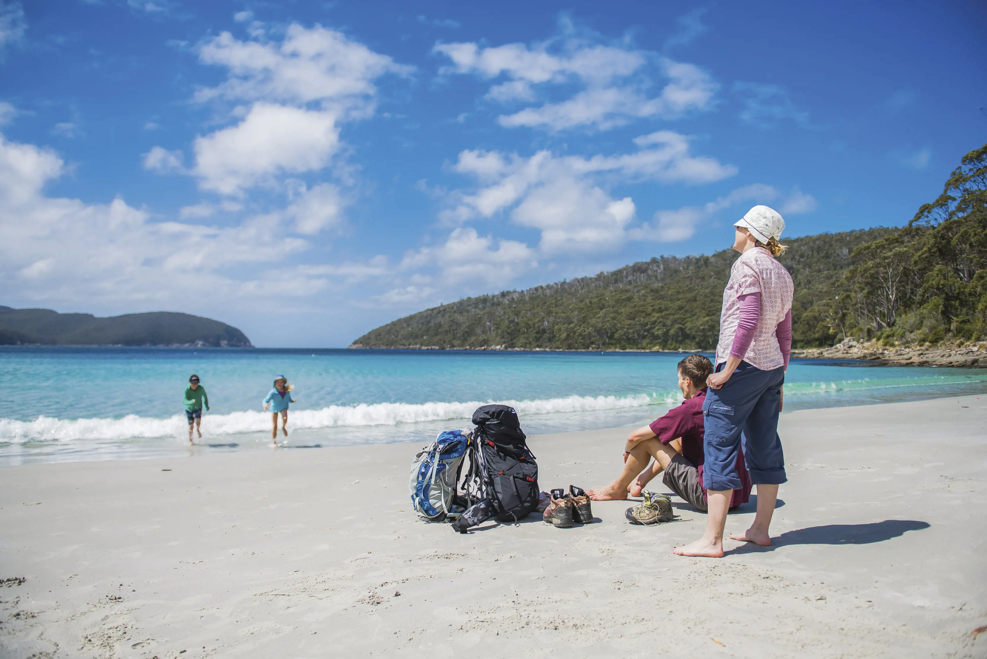 Children run from the sea towards their parents at Fortescue Bay, The Three Capes Track