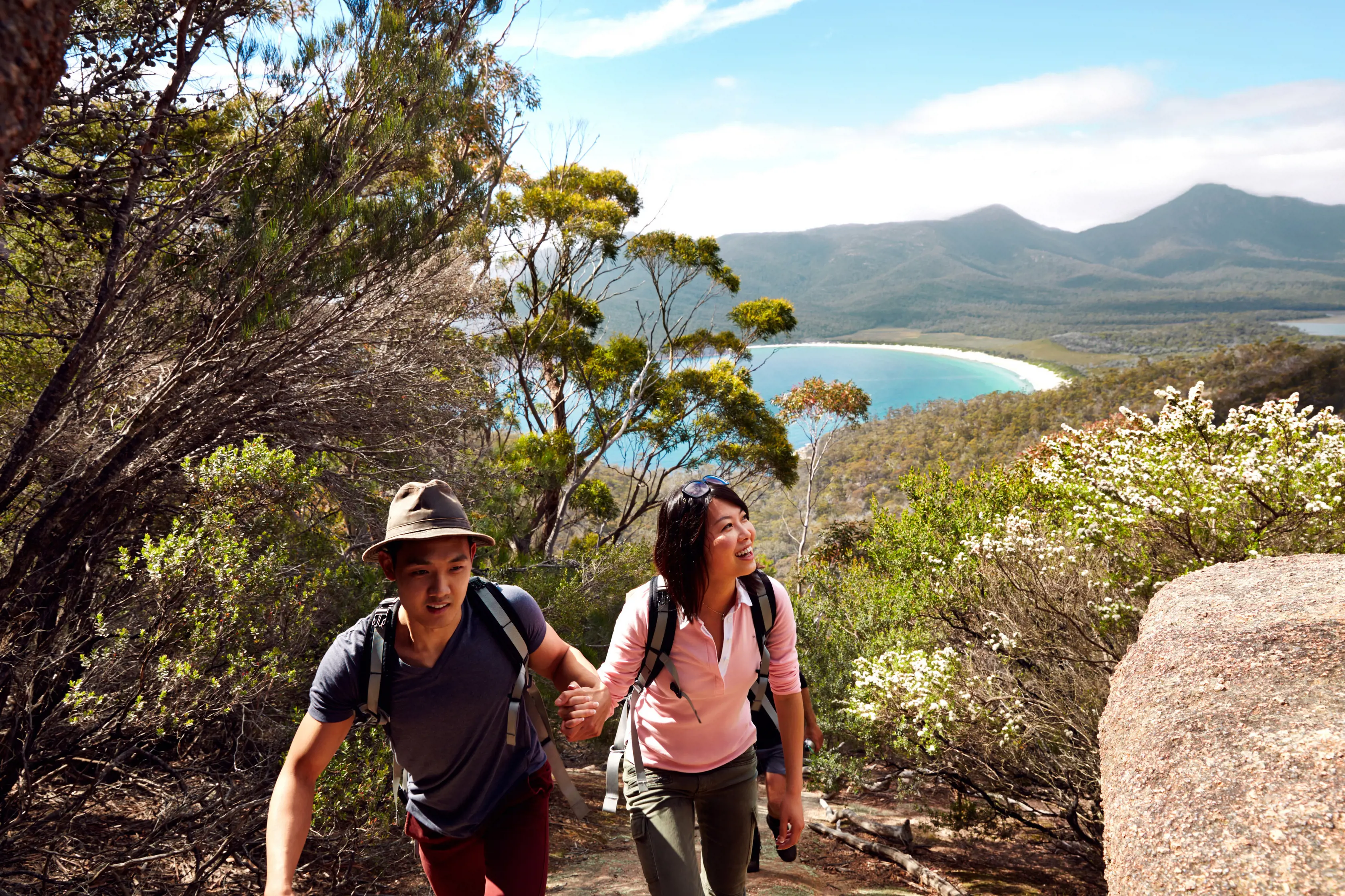 A couple climb to the lookout with views of Wineglass Bay in the background