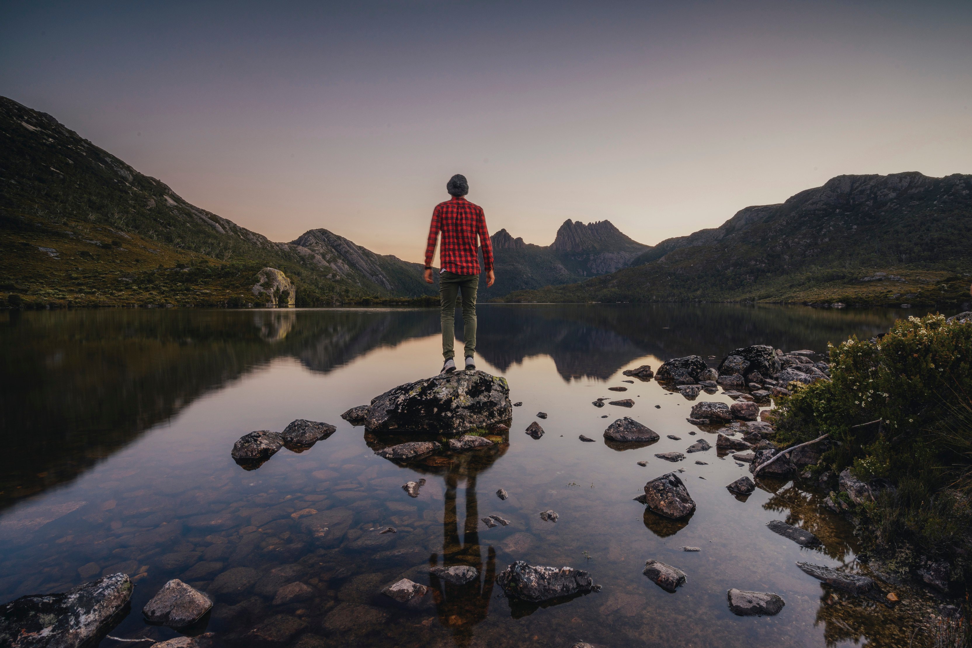 A man stands on a rock in the water looking at the views, Cradle Mountain