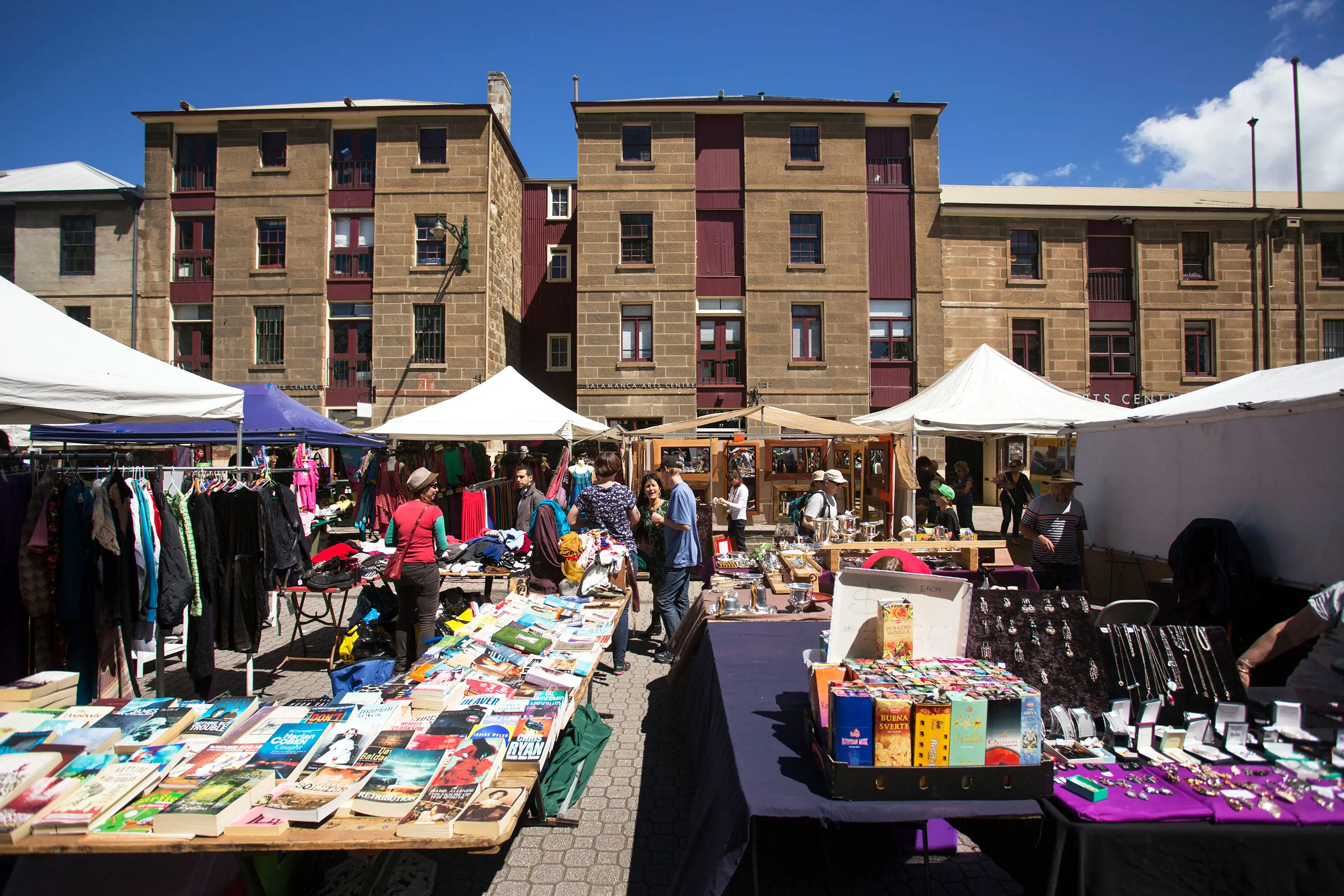 Market stalls with large tables display books, jewelry and oddments.