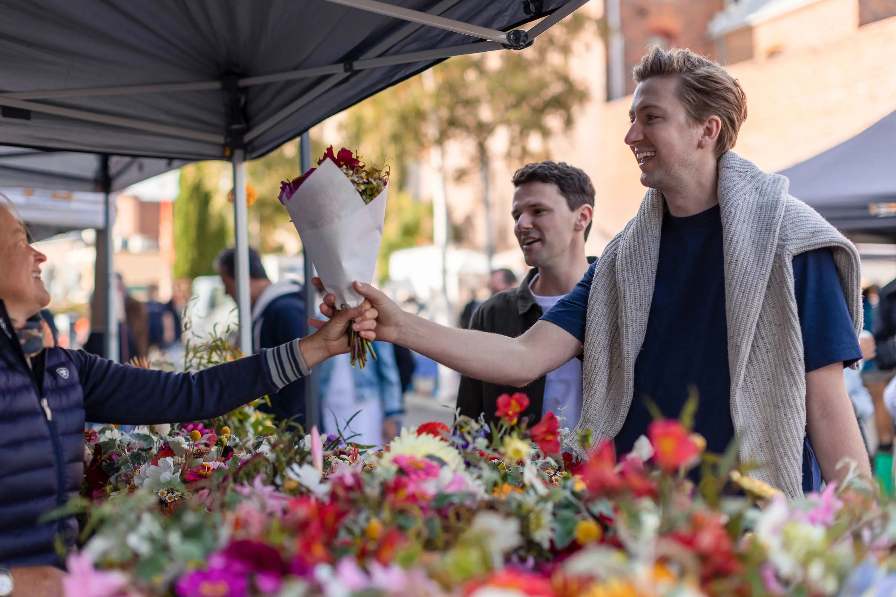 A man laughs with a stall holder while buying a large bouquet of flowers.