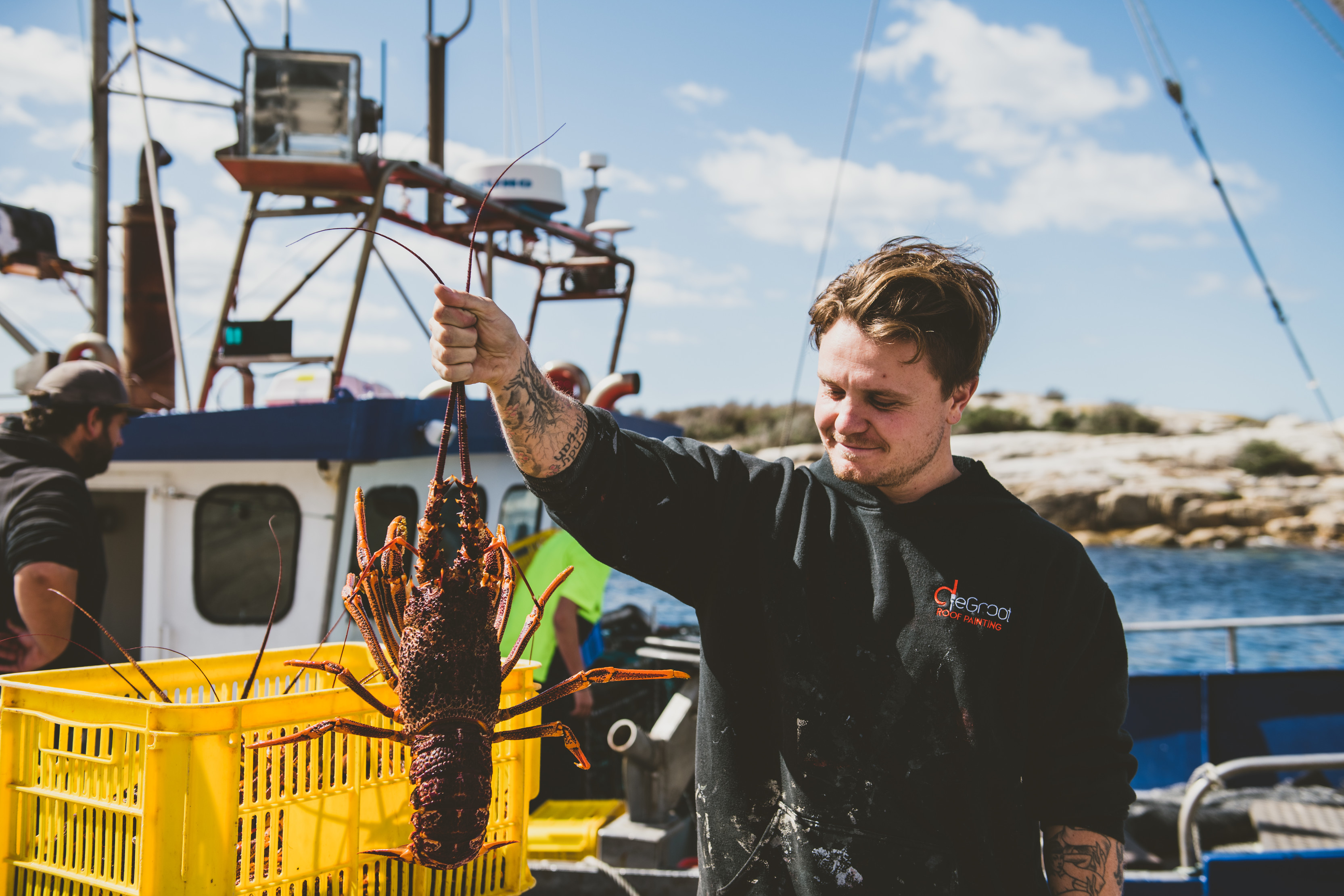 Person holding out a crayfish at the Bicheno wharf on a clear, sunny day.