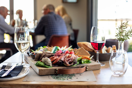 Image of a platter of a variety of fresh food accompanied with a bowl of bread and a glass each of red and white wine.