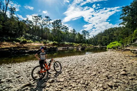 A cyclist stands by their bike by the water at Wild Mersey Mountain Bike Trails