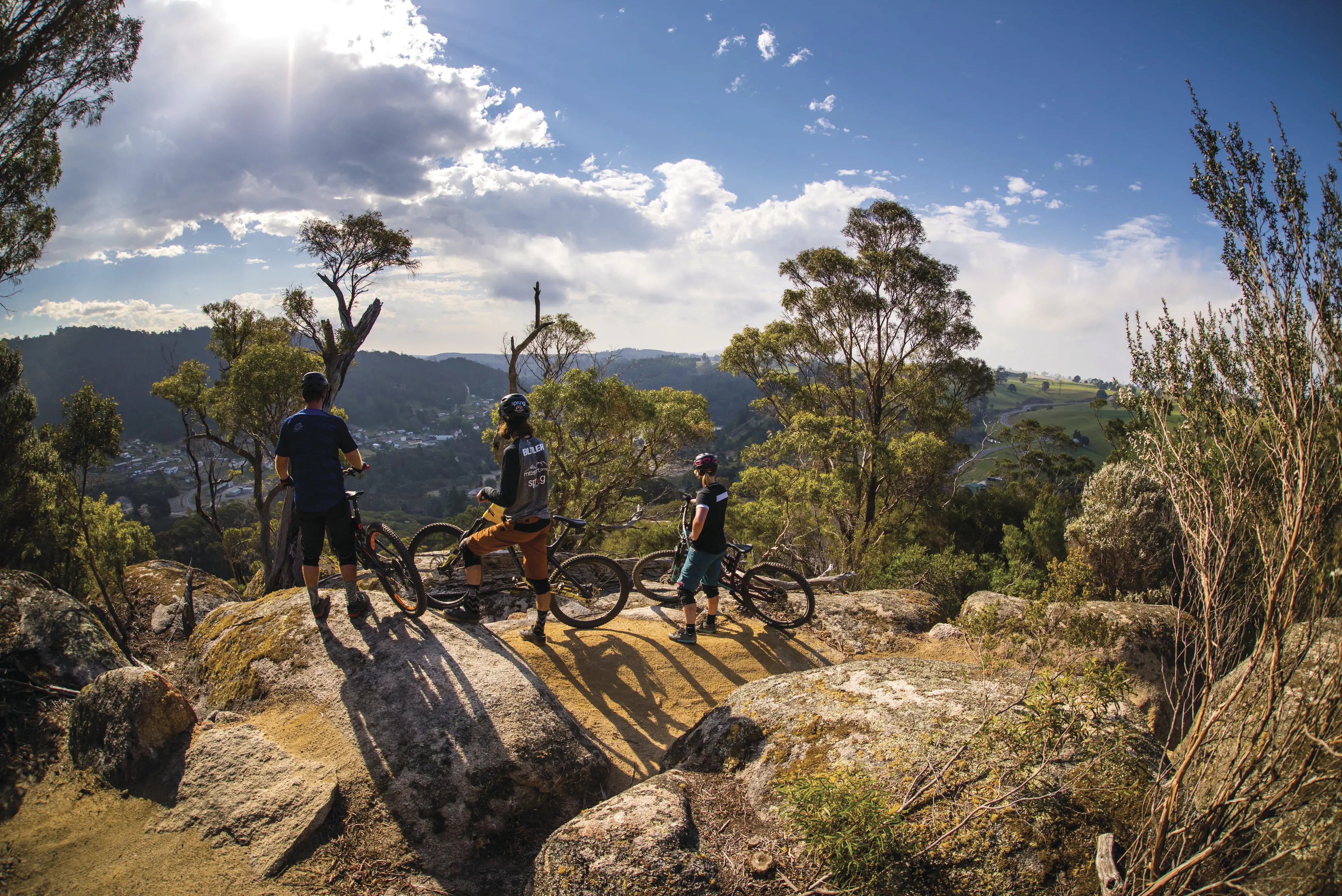 Wide angle image of four bike riders taking a break at a high peak, looking out into the wilderness, with Blue Derby Mountain Bike Trails.