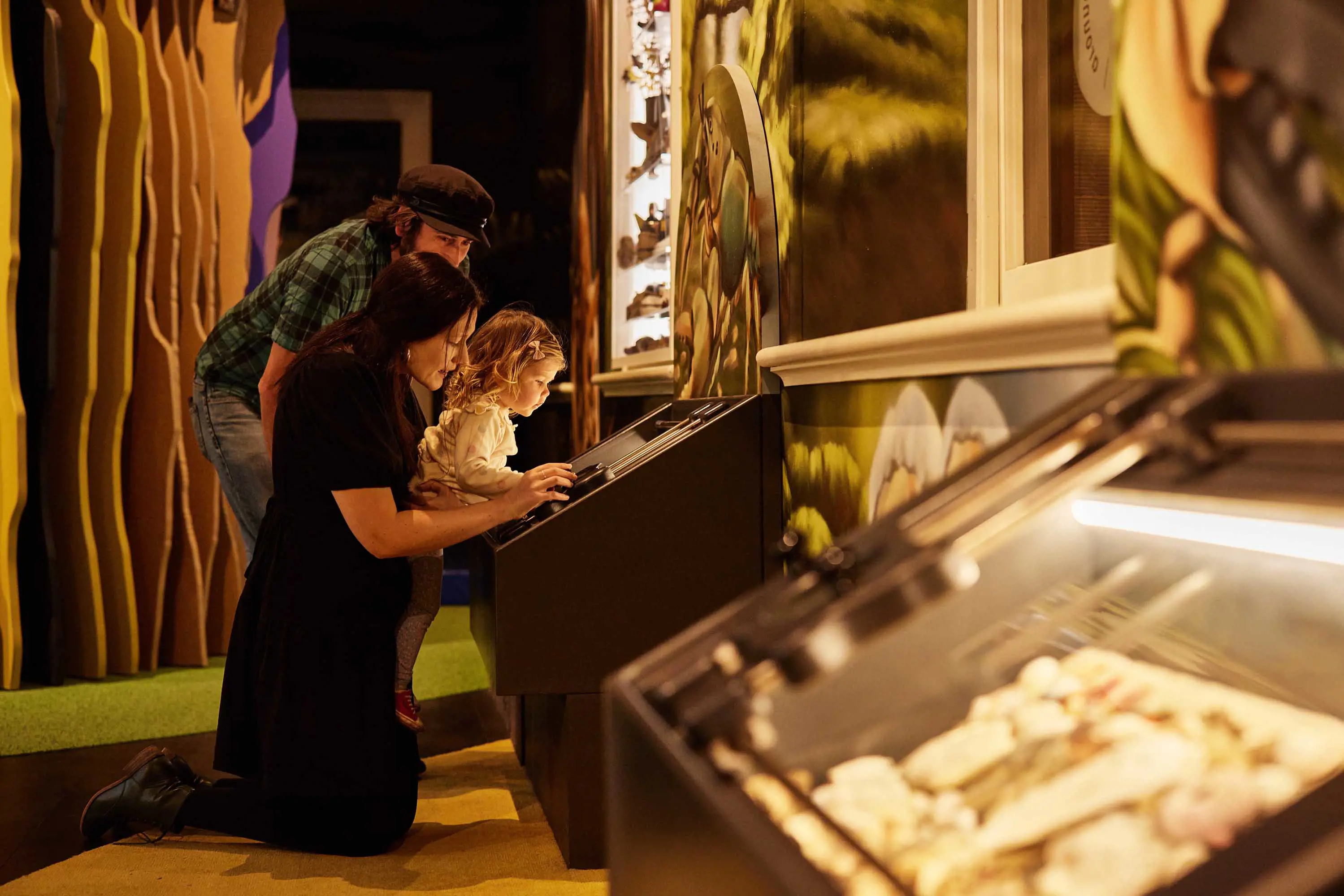 A young child looks at backlit displays with her mother and father.