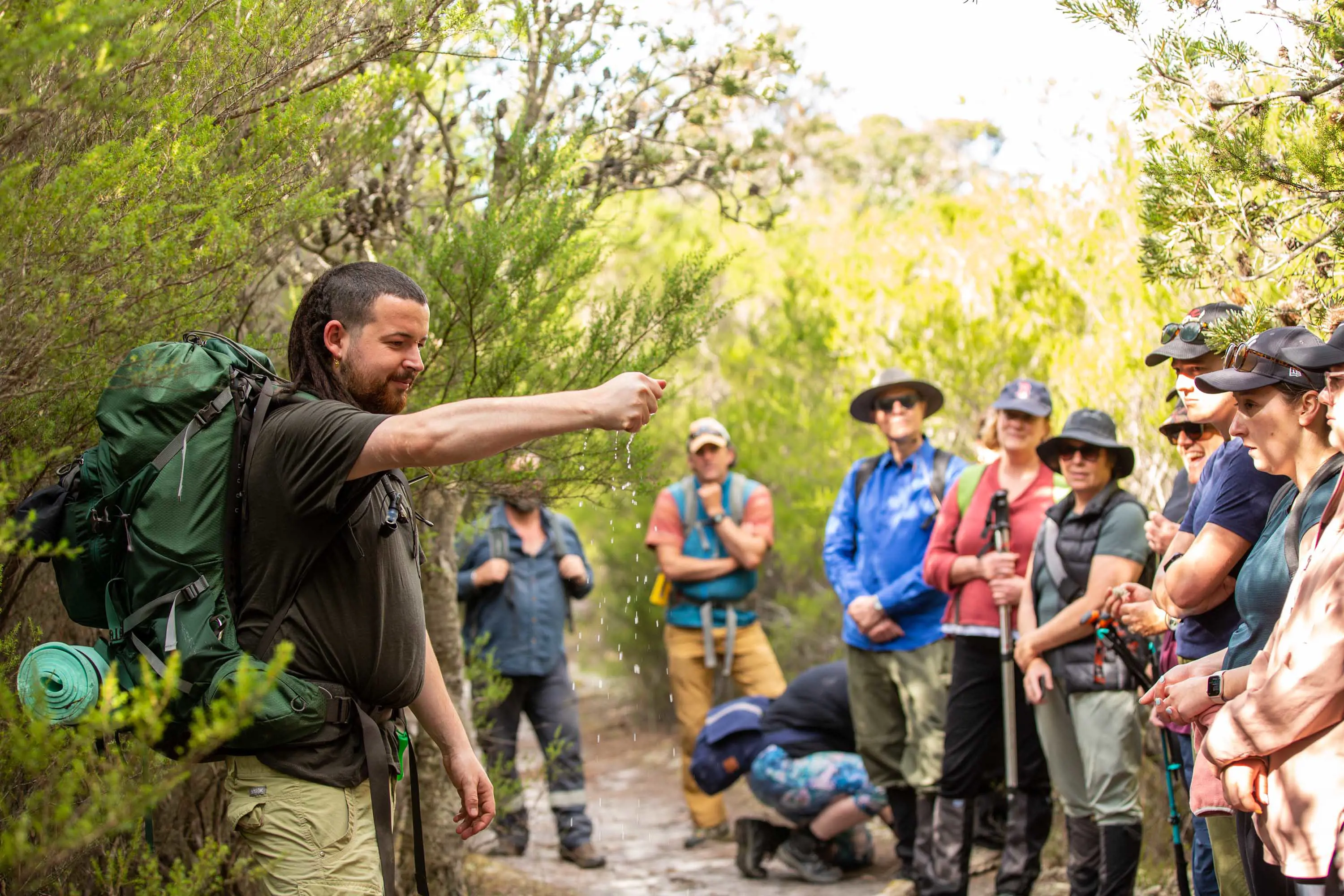 A man holds a demonstration in front of a group of hikers in dense bushland.