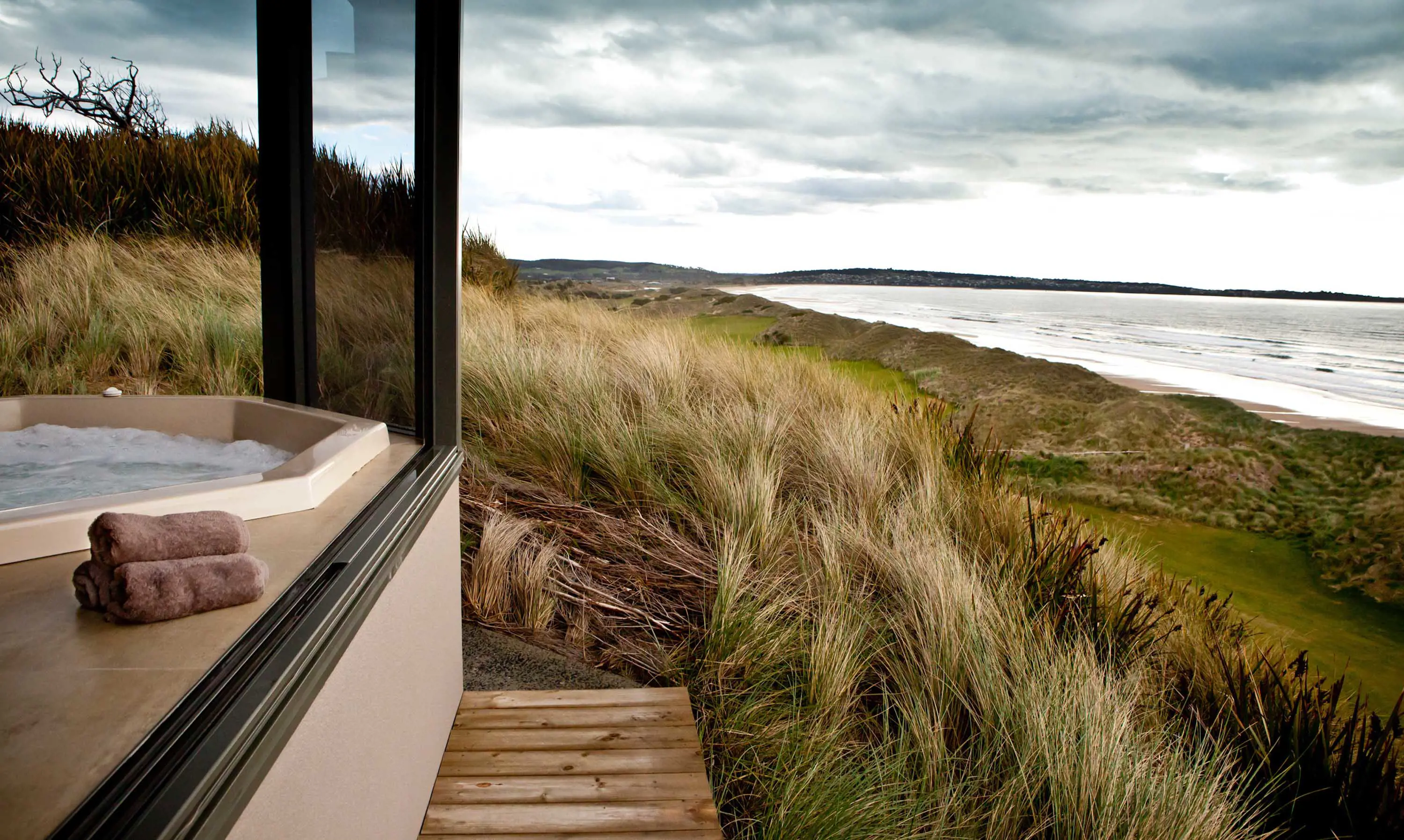 An enclosed spa looks out over a grassy coast with the ocean in the distance.