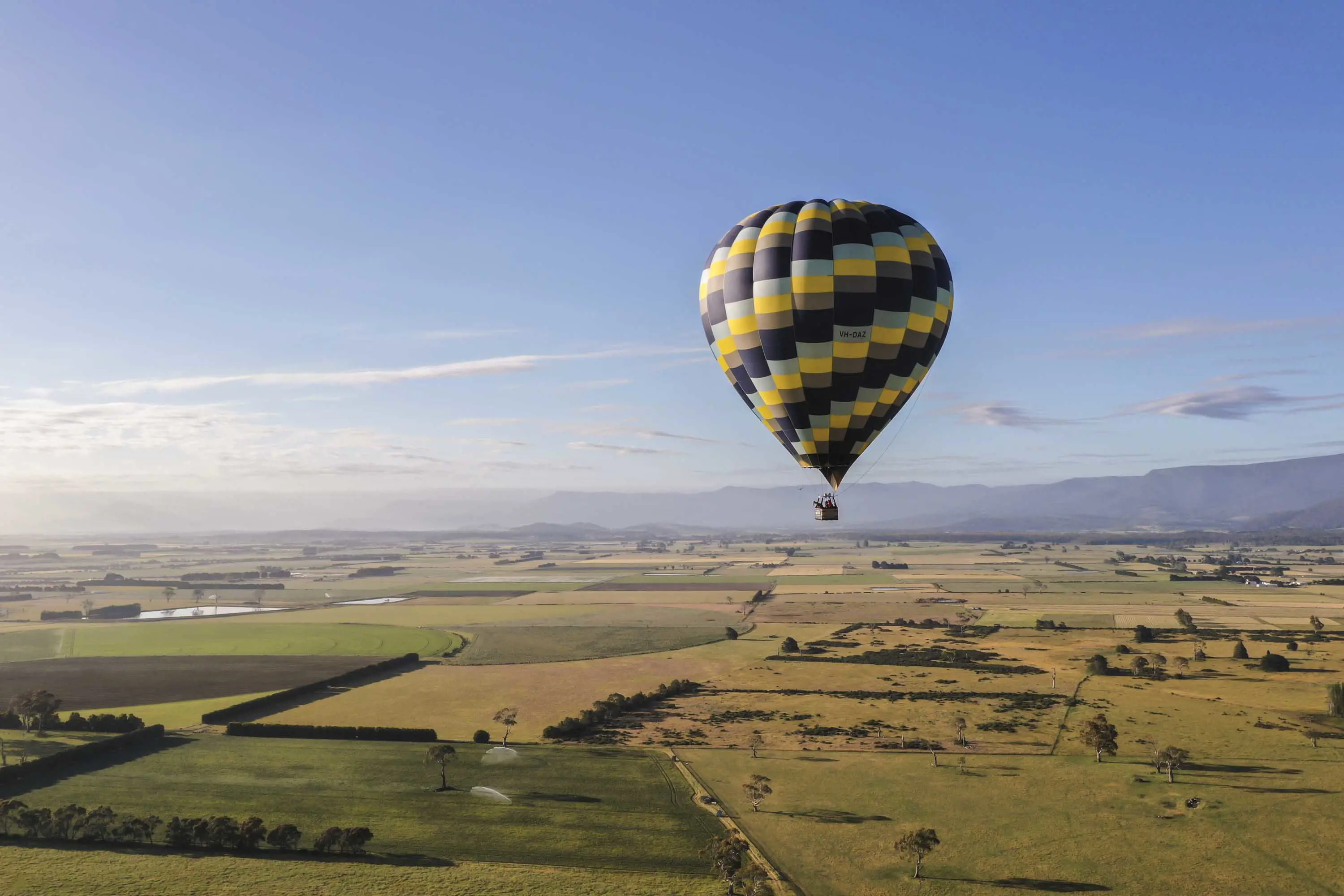 An enormous multicoloured balloon floats over farm land on a clear, sunny day.