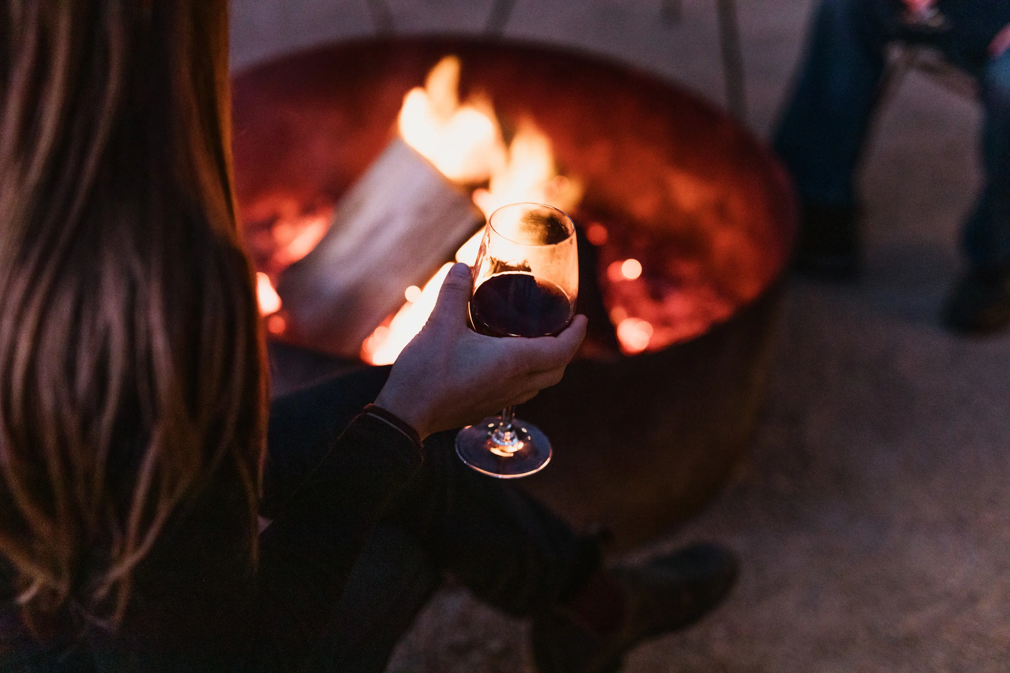 Woman holds a glass of red wine by the outdoor log fire at Bay of Fires Bush Retreat