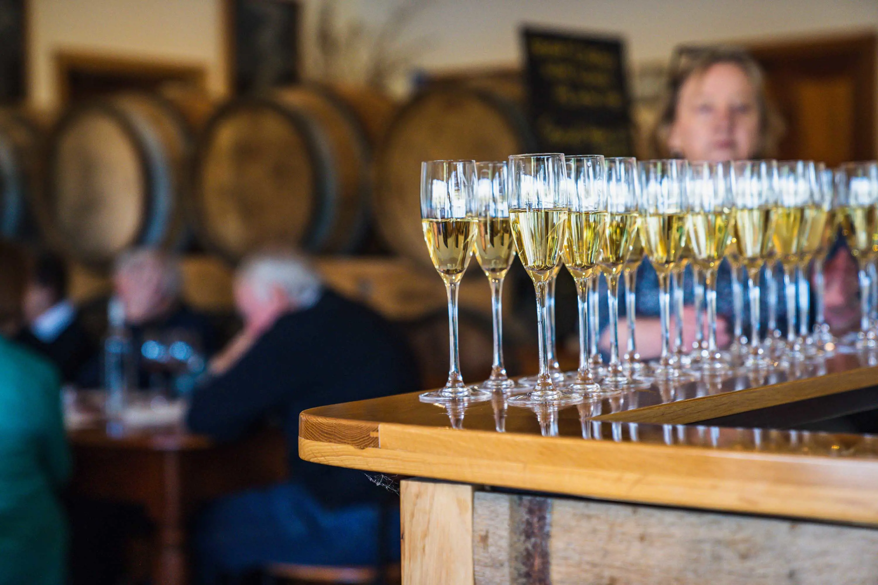 Rows of sparkling wine glasses filled with wine stand on a wooden bar in a tasting room. 