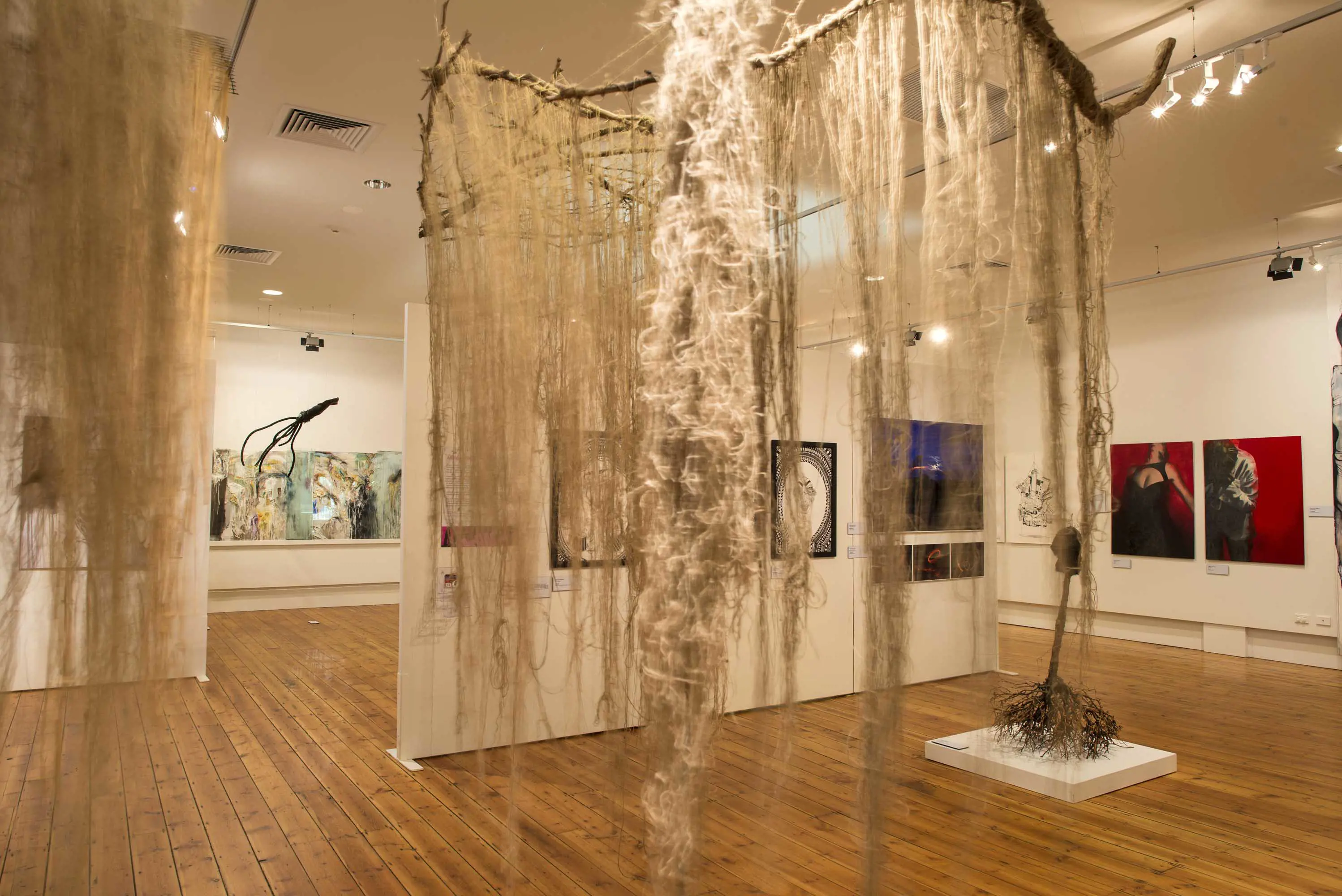 An artwork made from twine hangs from the ceiling of a gallery space with polished floorboards.